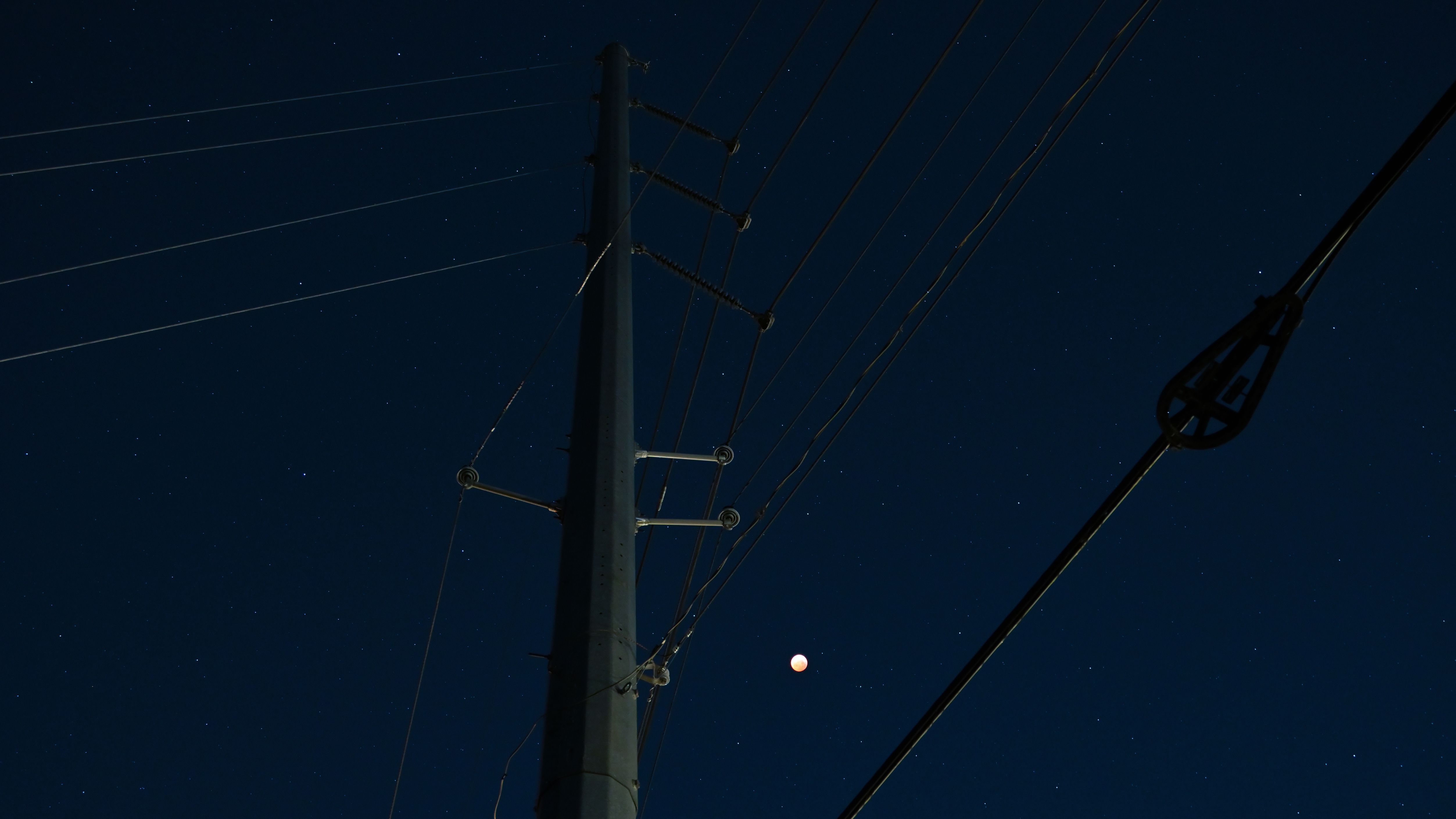 Tall utility pole with power transmission lines against a night sky with a full moon