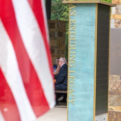 Teal monument pillar with gold lettering and an American flag in the foreground.