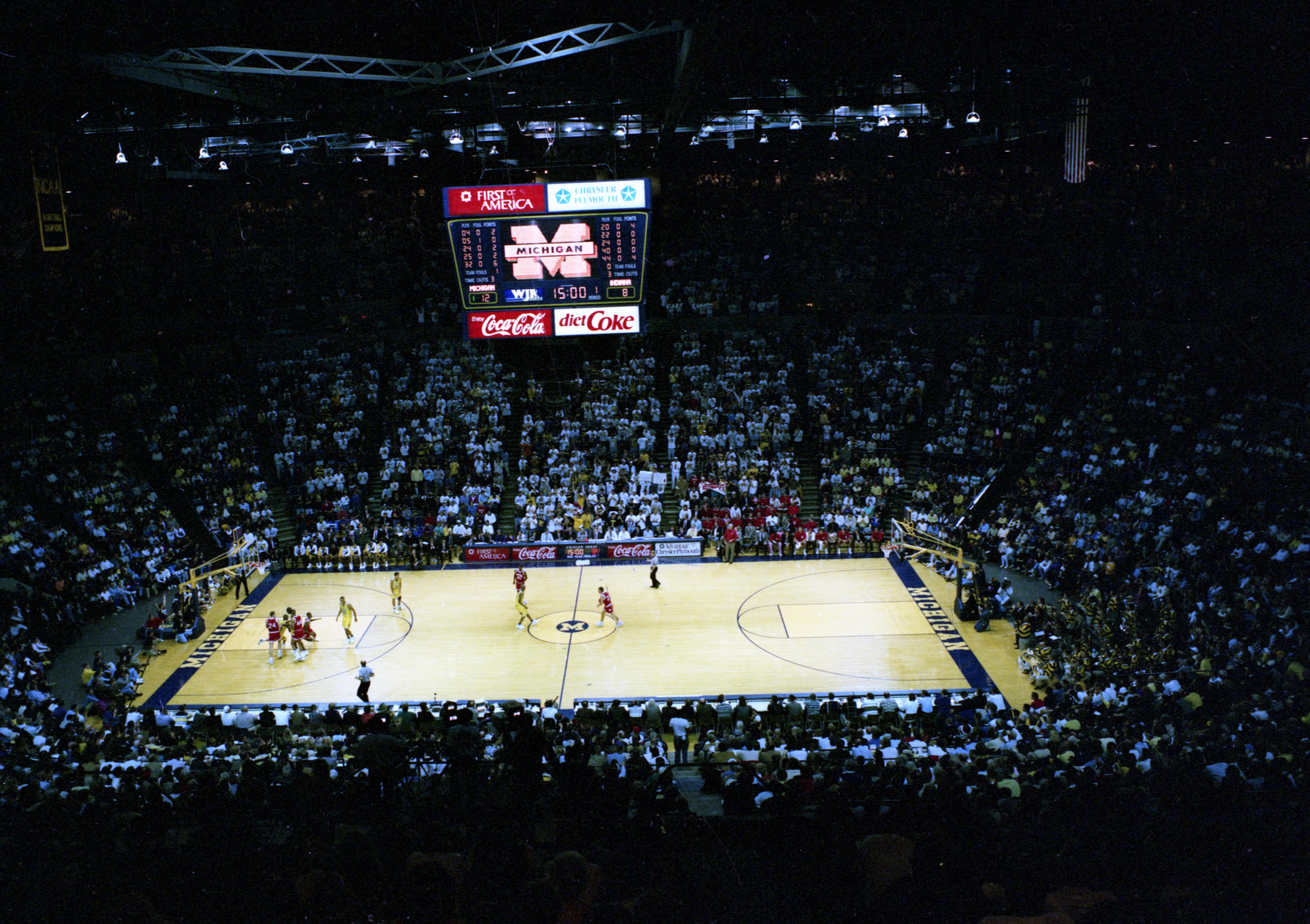 Overhead view of a packed basketball arena with players on the hardwood court below.