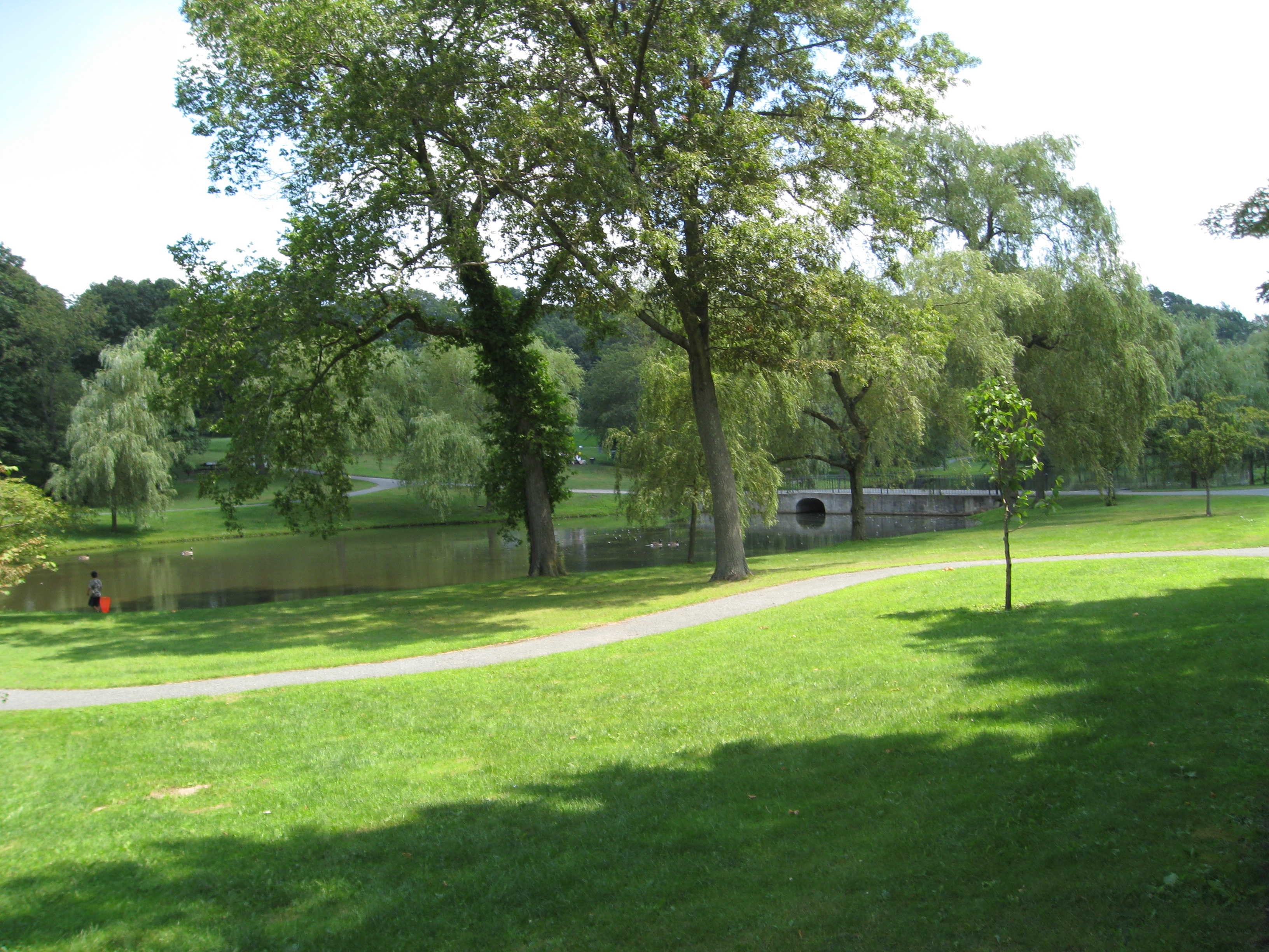 A green park with a stone bridge over a lagoon, walking paths, and mature trees.