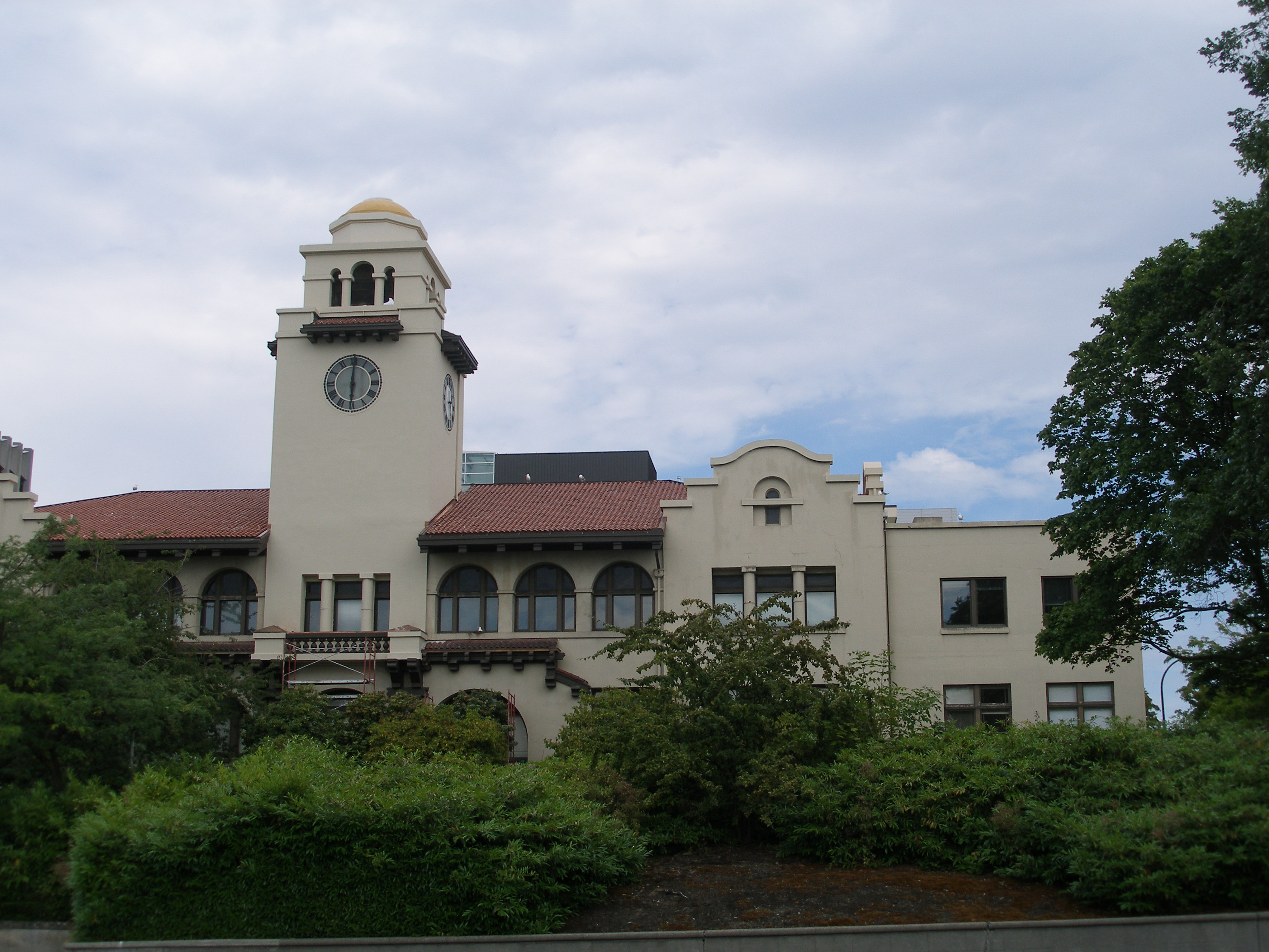Cream-colored historic courthouse with a domed clock tower and arched windows amid trees.