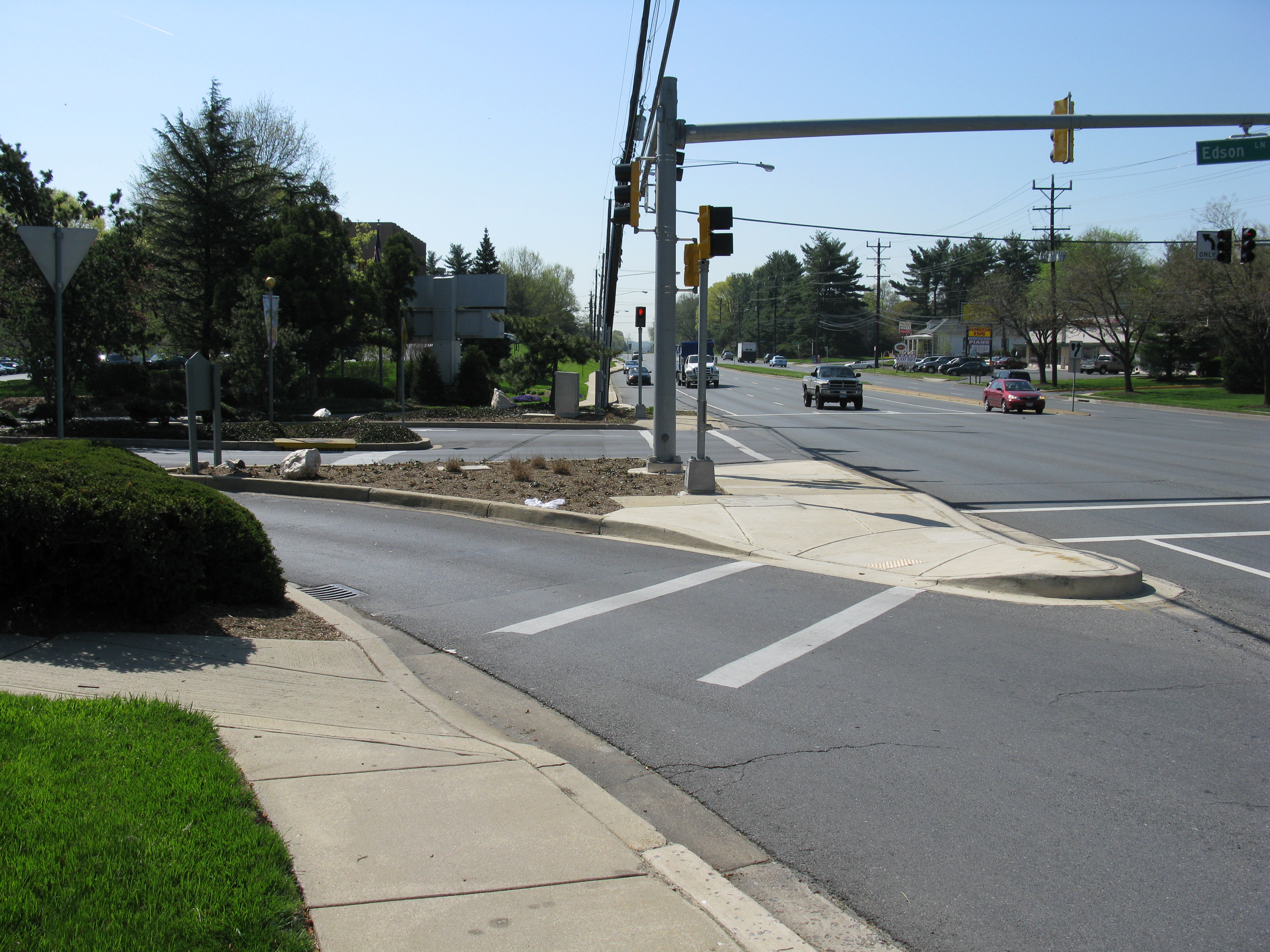 Multi-lane suburban road with crosswalks, overhead traffic signals, and a sidewalk curb ramp.