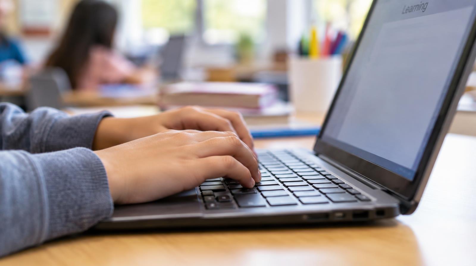 Small child's hands resting on a laptop keyboard, fingers on home row keys.