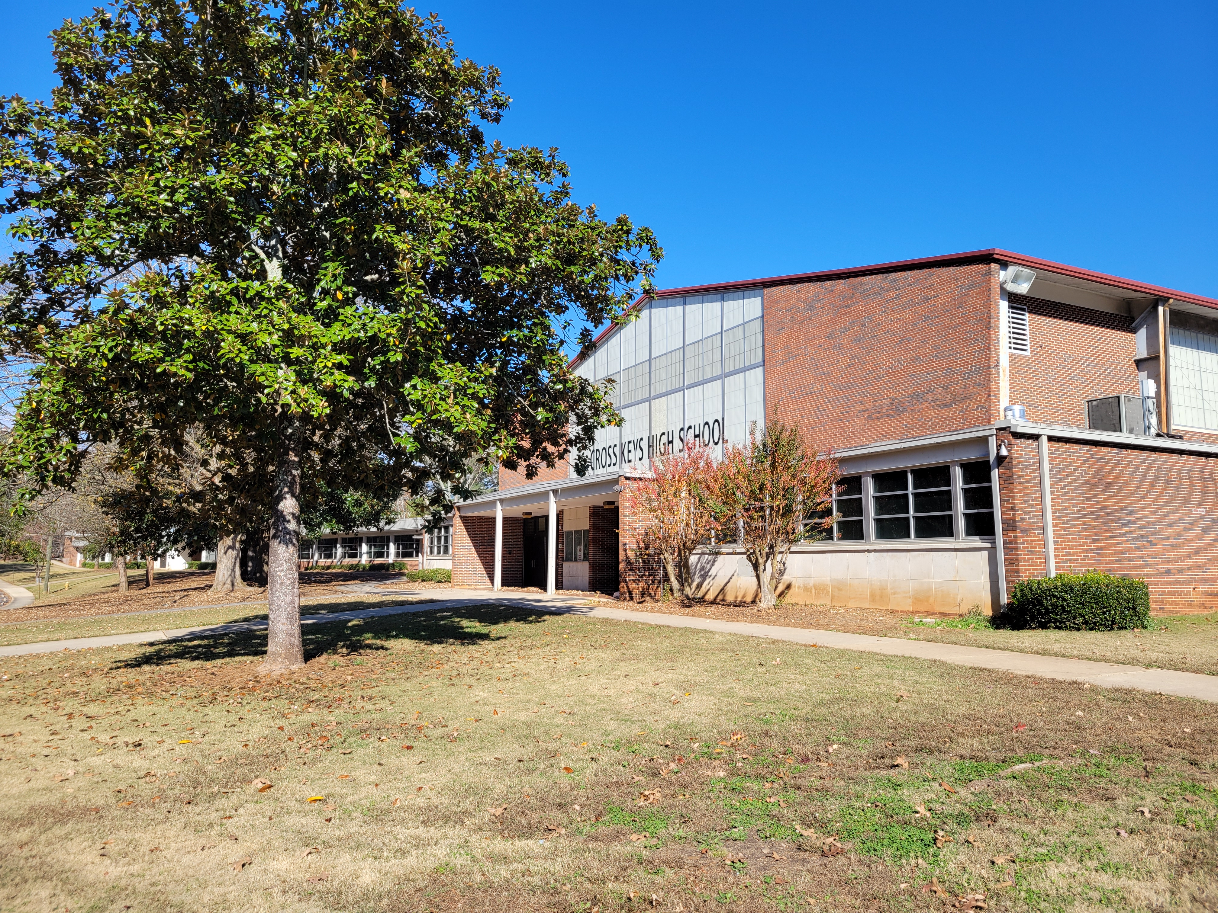 Brick school building with a metal facade panel reading Cross Keys High School, under a clear blue sky.