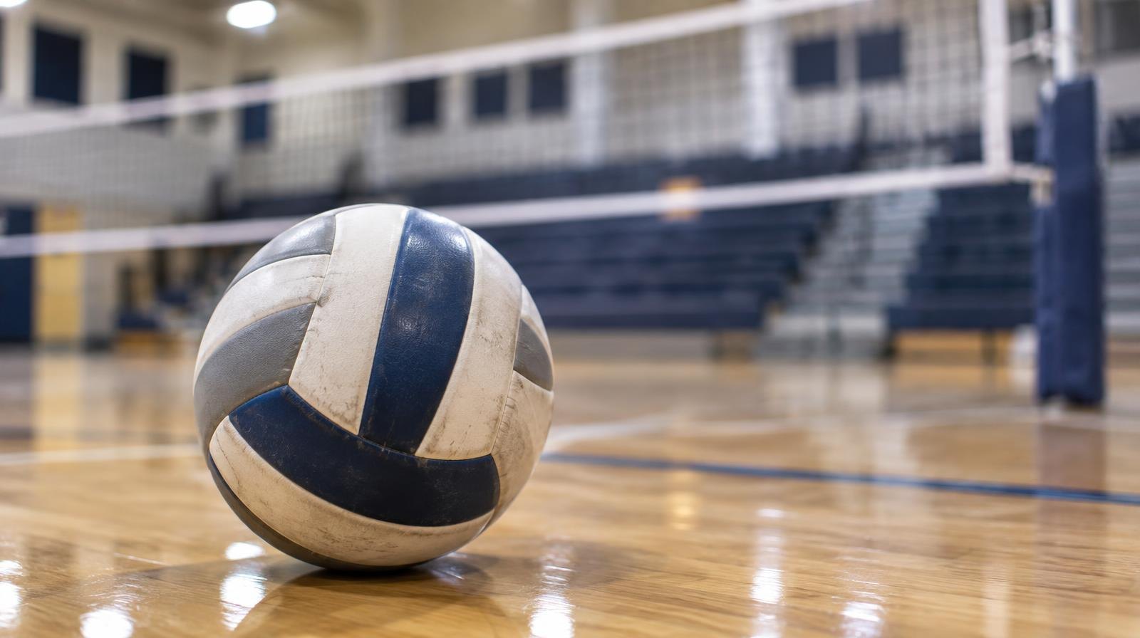 A volleyball resting on a hardwood gymnasium floor near the net.
