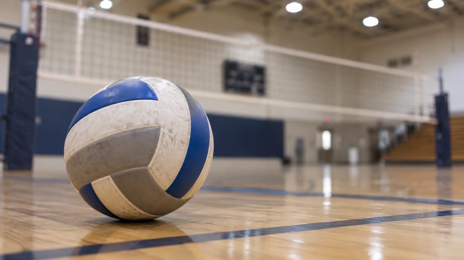A volleyball resting on a hardwood gymnasium floor near a net.