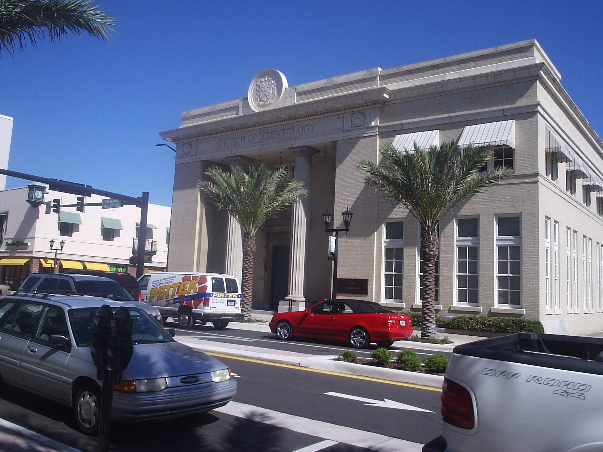 Neoclassical stone building with columns and palm trees on a sunny downtown street.