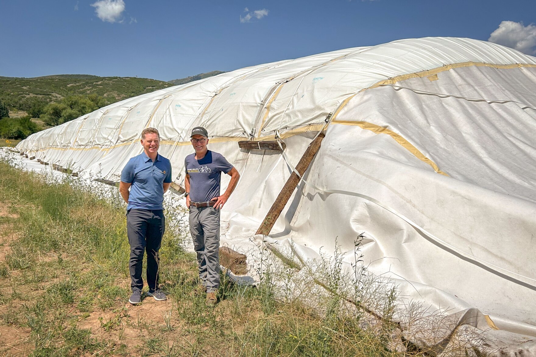 Two men stand outdoors in front of a large mound covered in white insulating fabric.