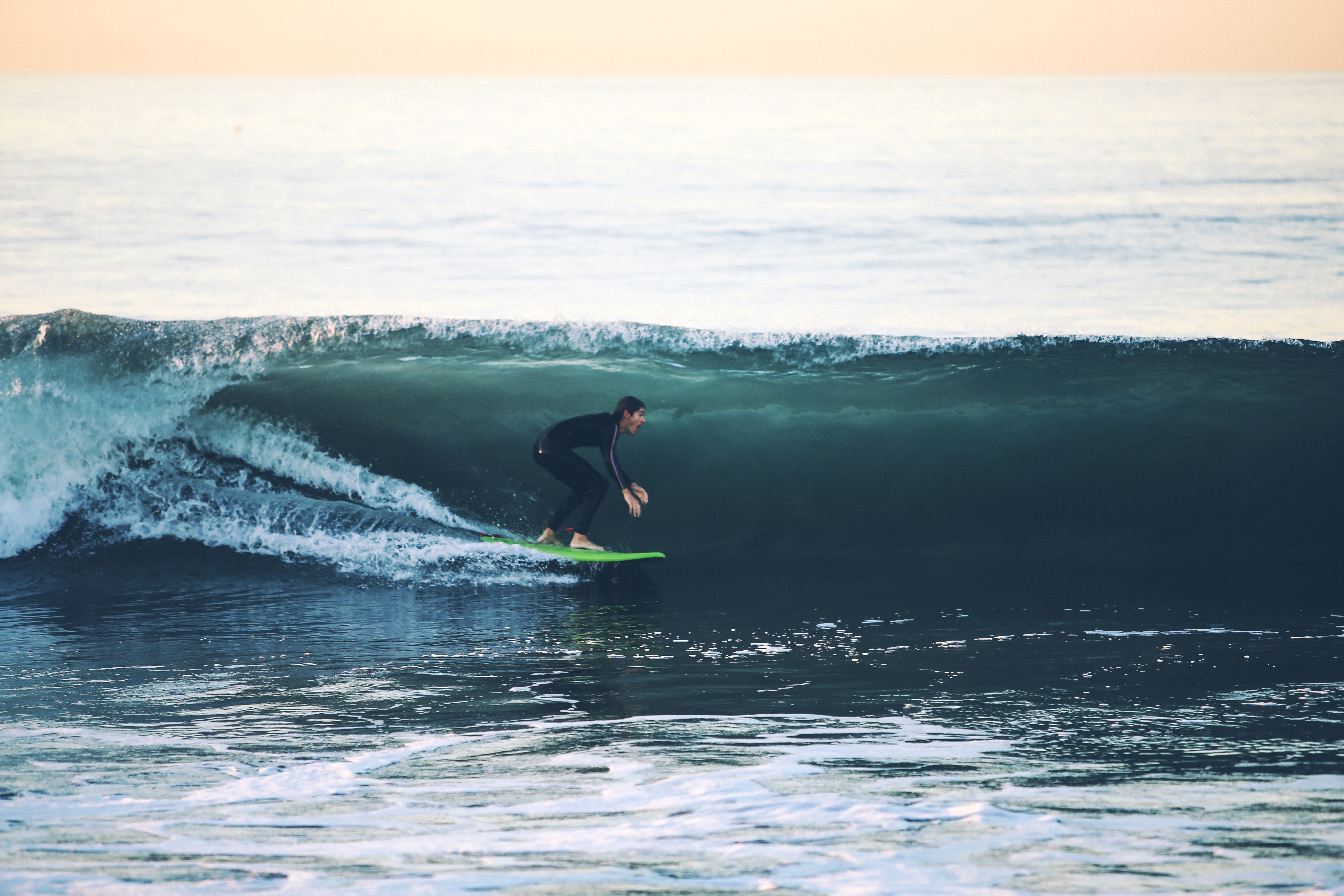 Surfer in a black wetsuit rides a large curling ocean wave on a green surfboard.