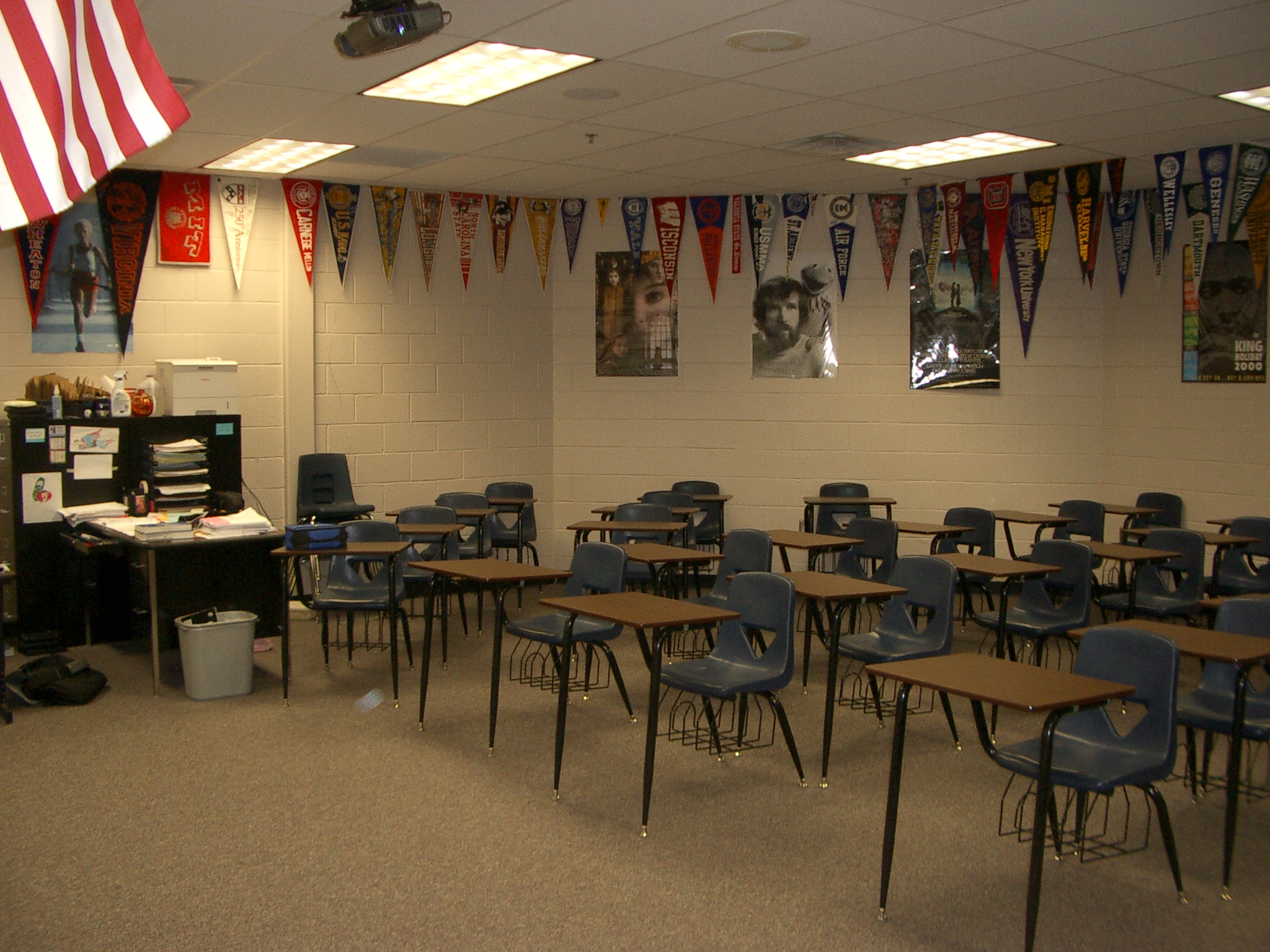 Empty high school classroom with rows of student desks and college pennants on the walls.