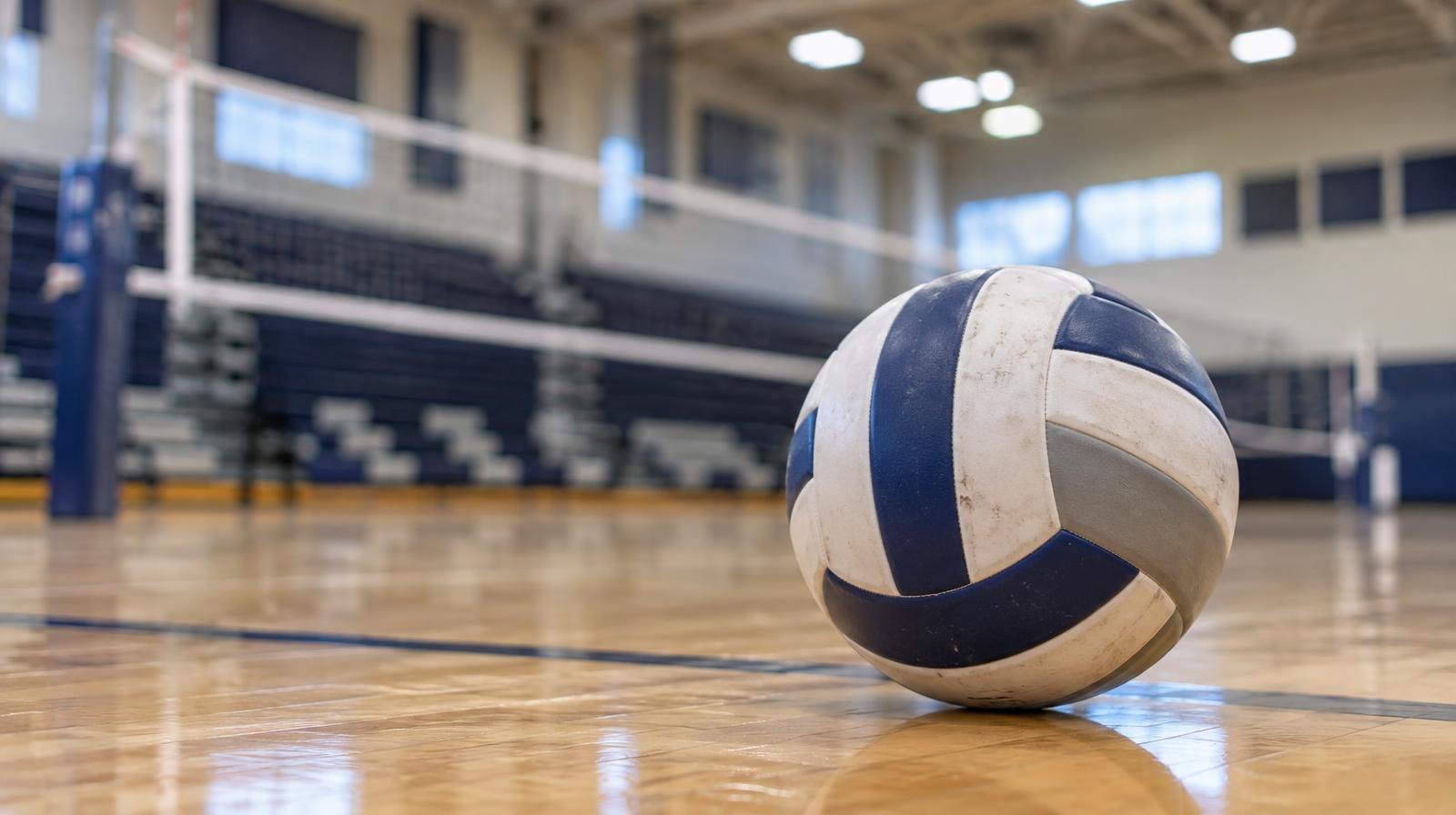 A volleyball resting on a hardwood gymnasium floor near the net.