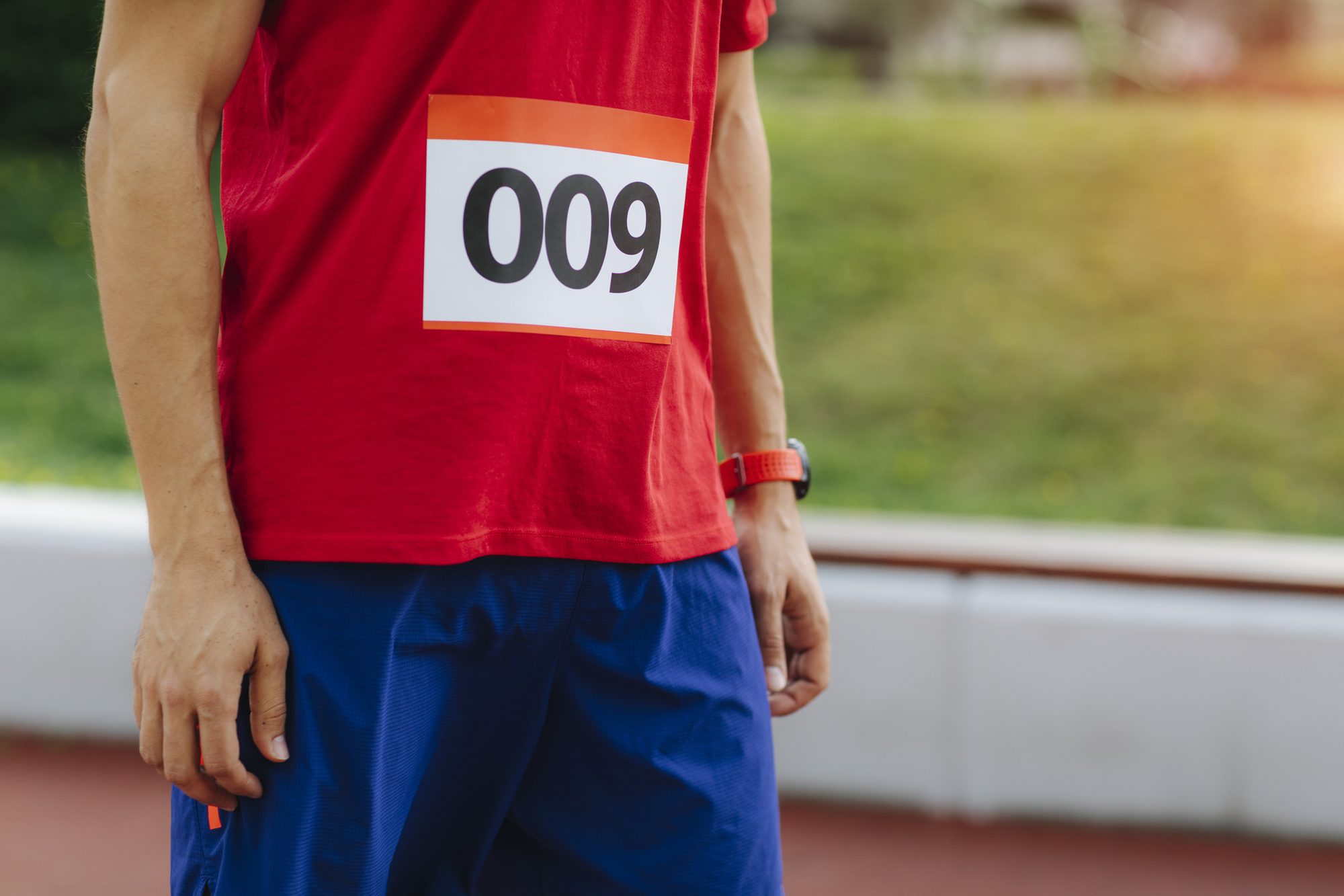 Runner wearing a race bib numbered 009 standing at an outdoor track ahead of a 5K run.