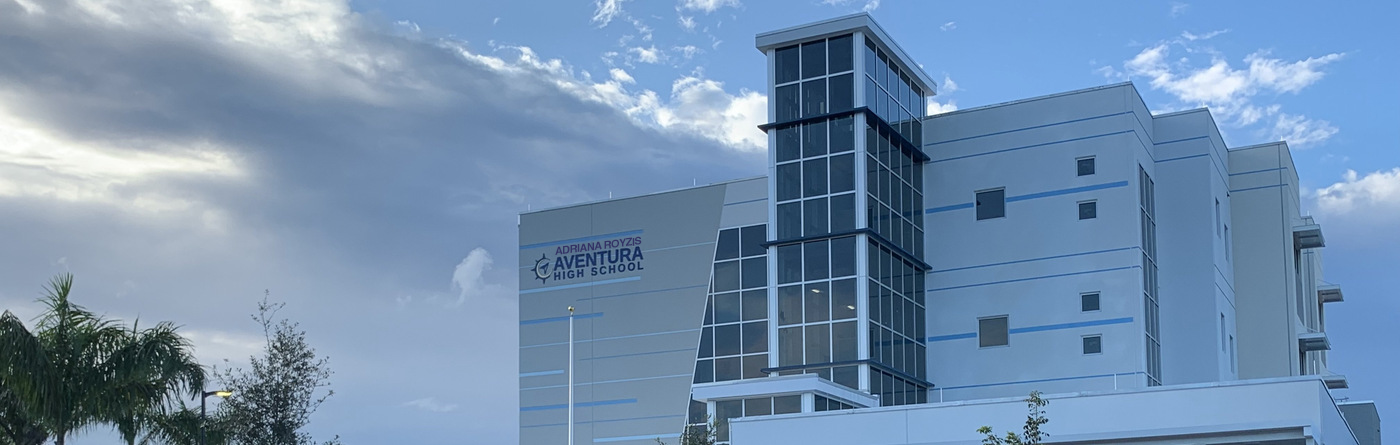 Modern white multi-story school building with large glass windows and school name on facade.