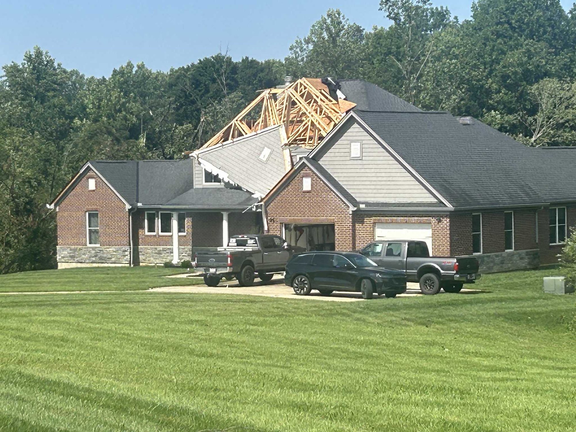 Brick ranch home with roof torn away, exposing wooden trusses, after a storm.