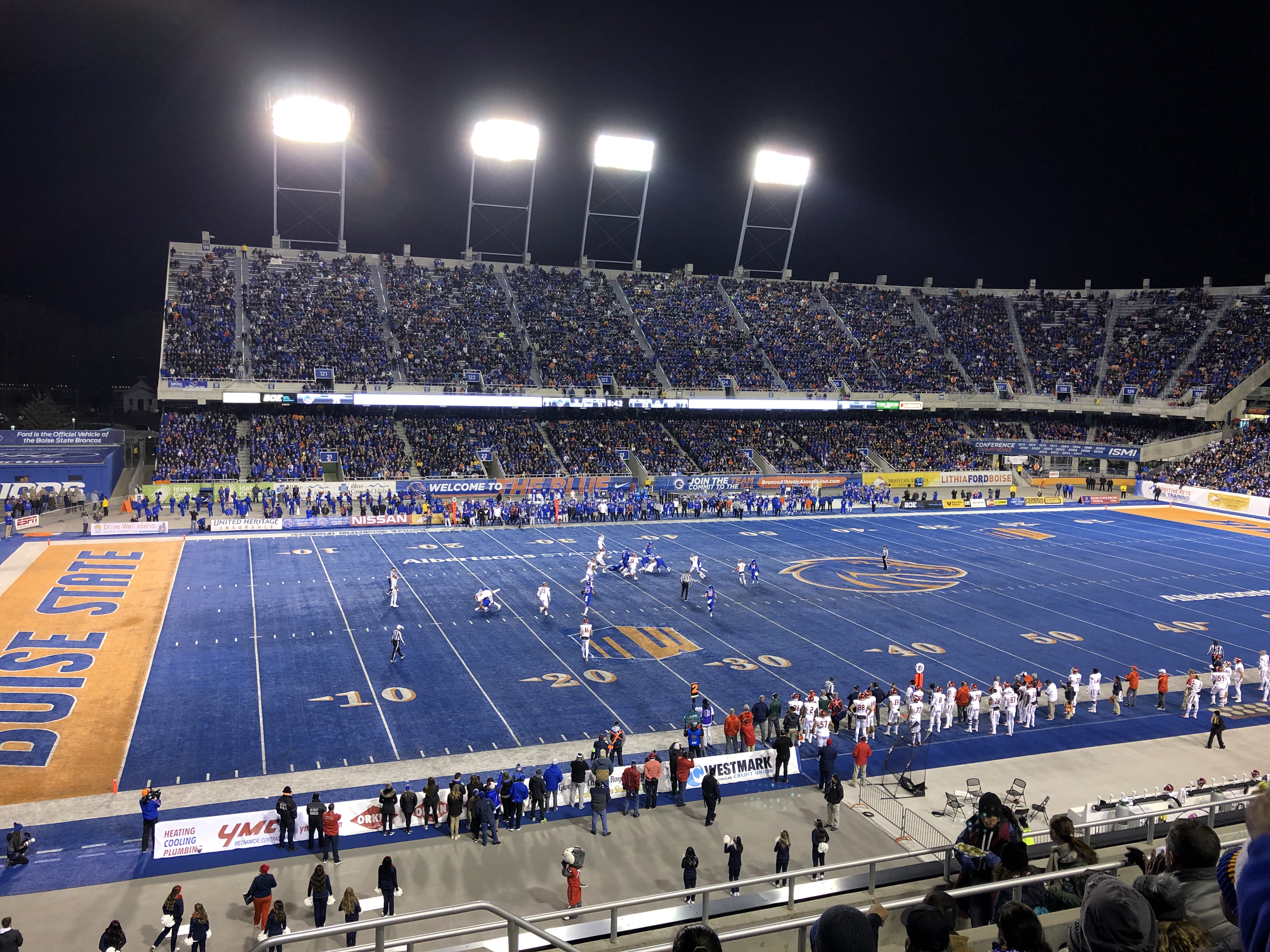Boise State football stadium at night with blue turf and stadium lights.