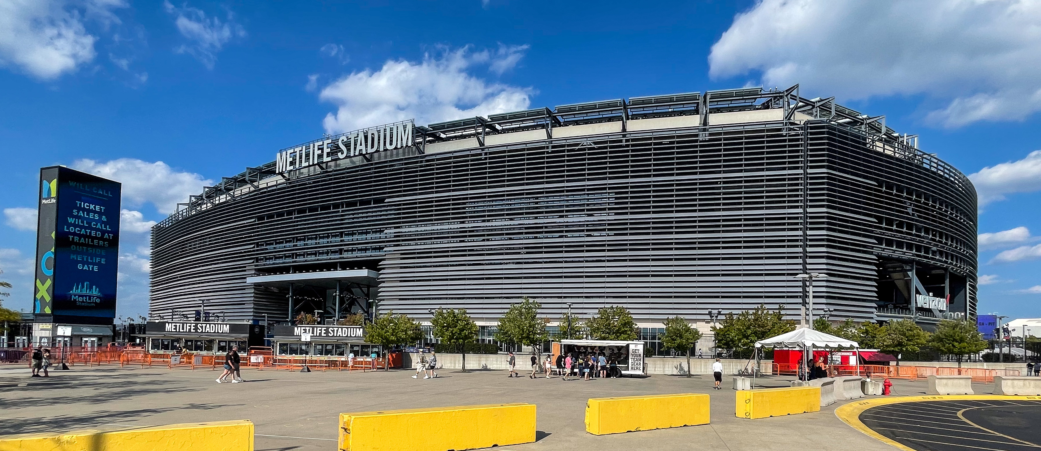 Wide exterior view of MetLife Stadium with yellow barriers and a digital sign.