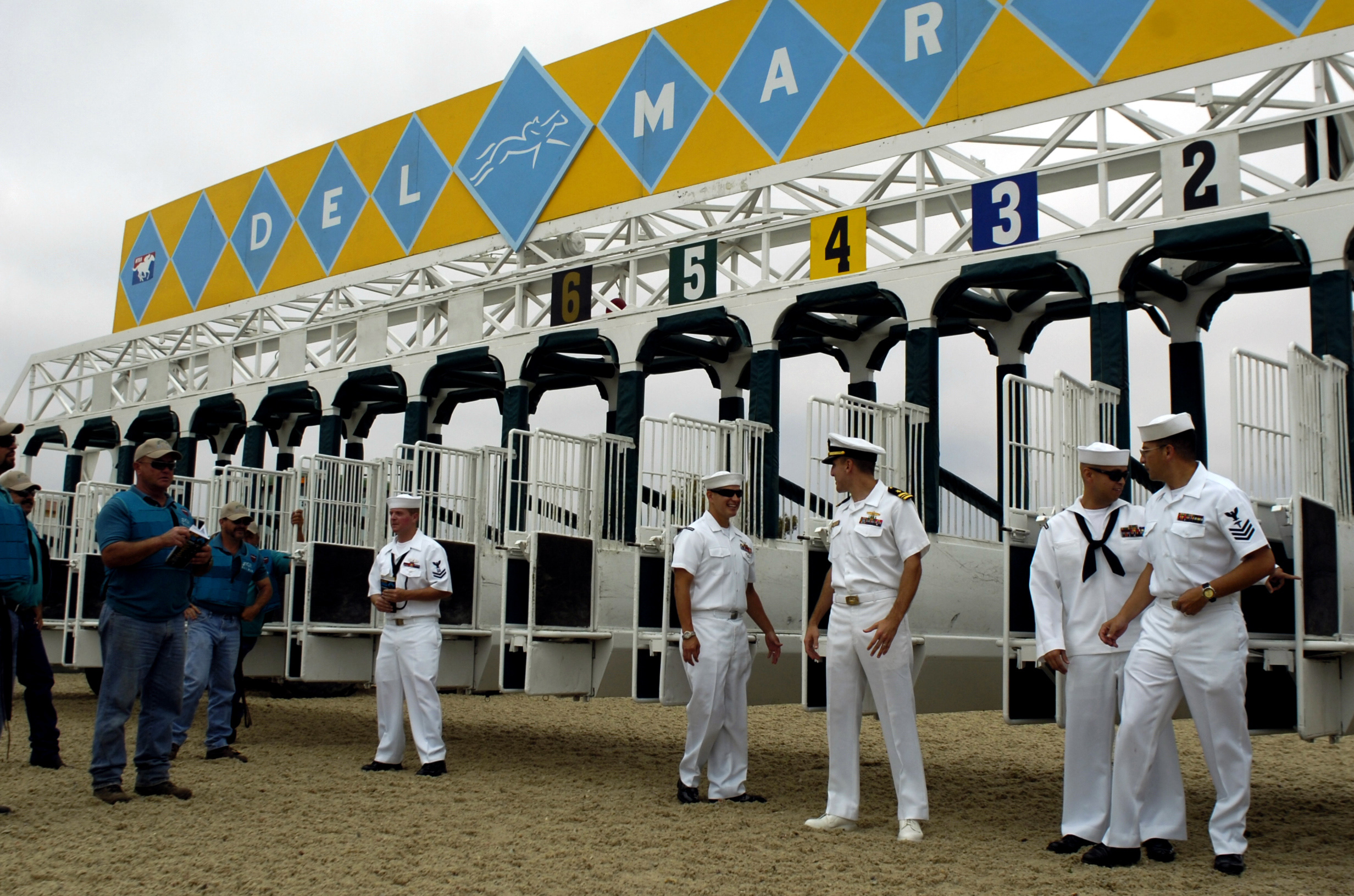 Numbered starting gate stalls on a dirt track with Del Mar signage overhead.