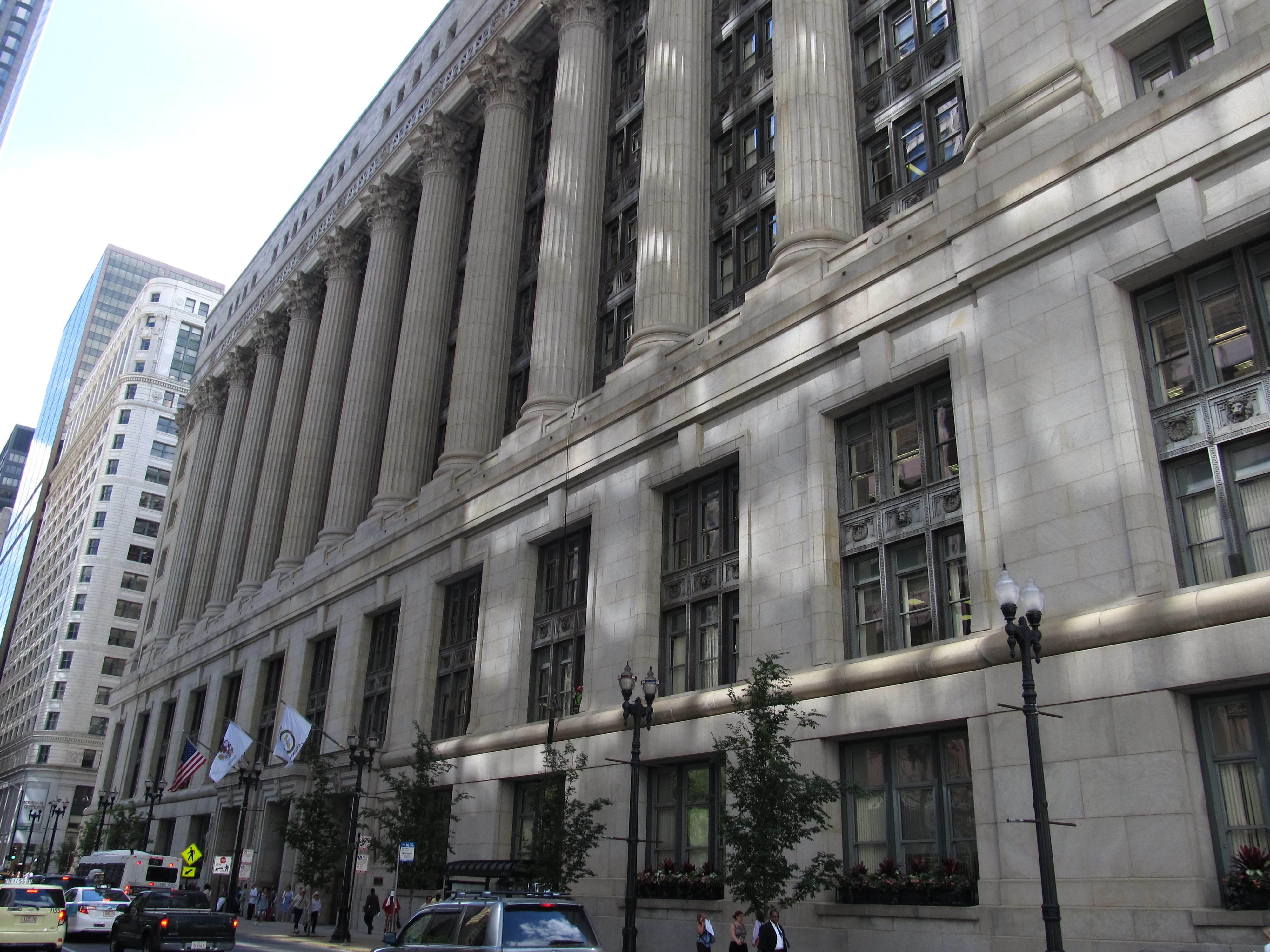 Classical revival stone government building with tall columns along a city sidewalk.