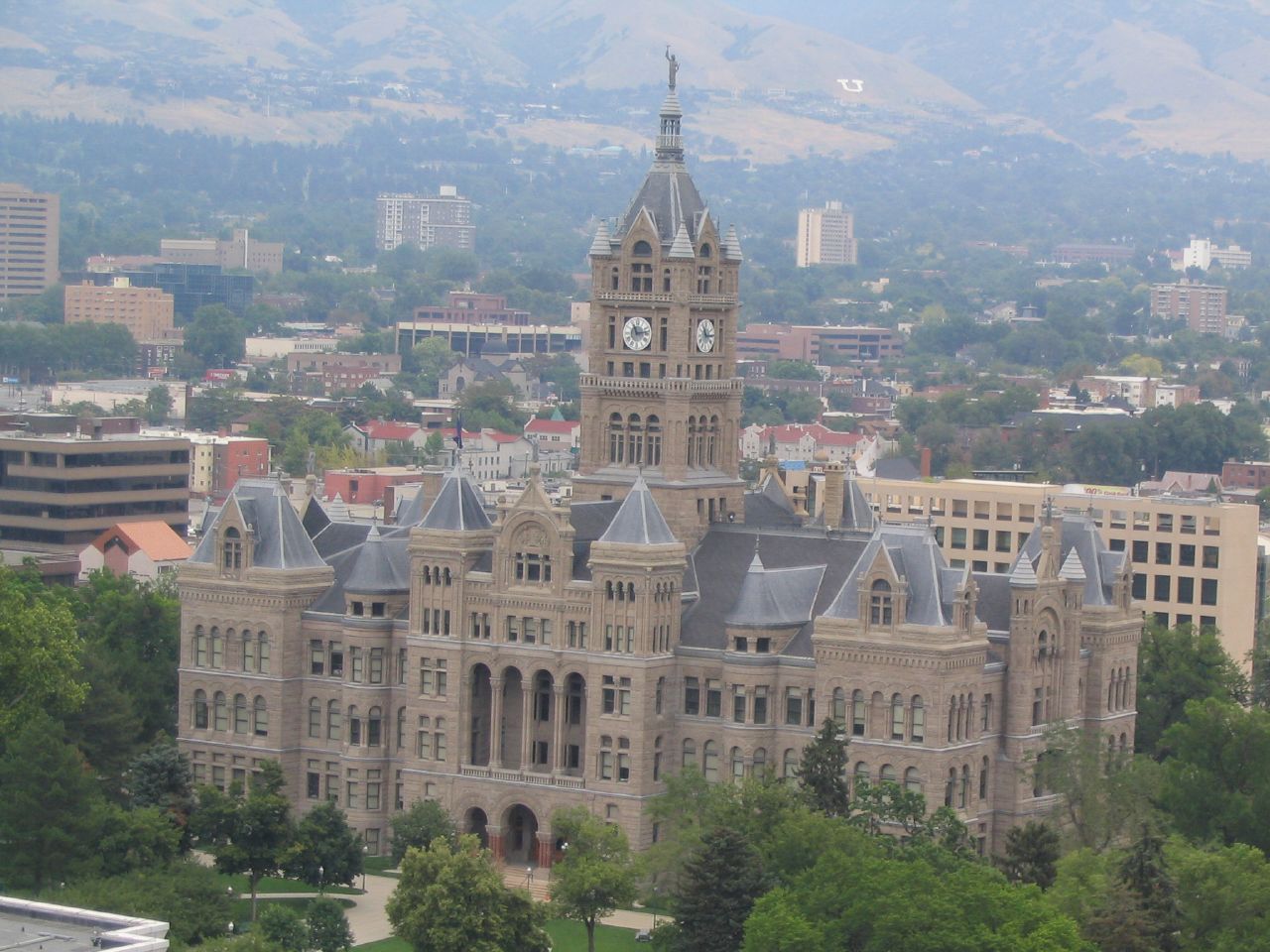 Ornate sandstone government building with a tall central clock tower, surrounded by trees and city blocks.