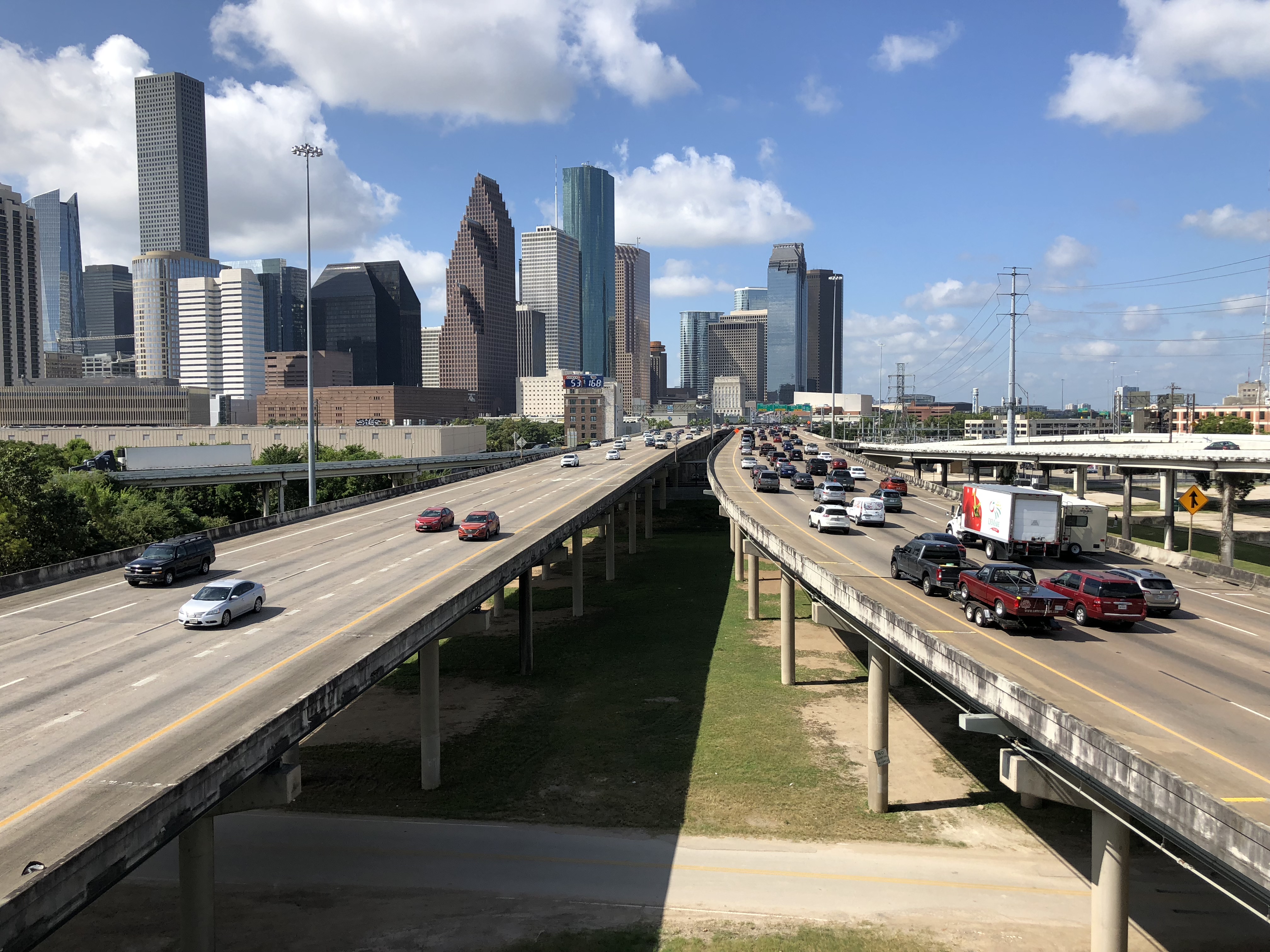 Multi-lane freeway stretching toward a city skyline under partly cloudy skies.