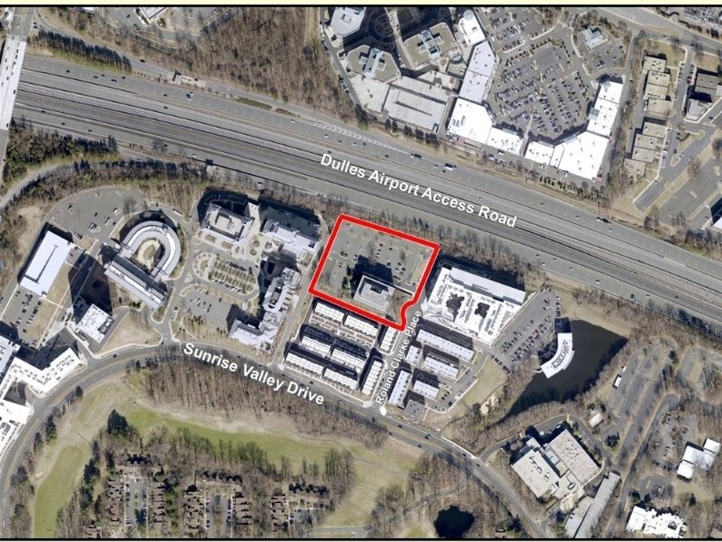 Aerial satellite map showing a property parcel outlined in red between a highway and surrounding office buildings.