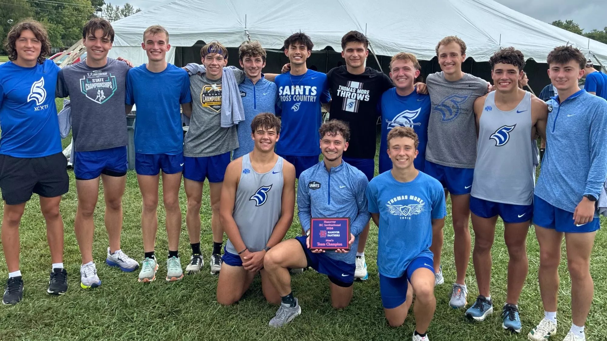 Group of male athletes in blue uniforms posing outdoors with a small award plaque.