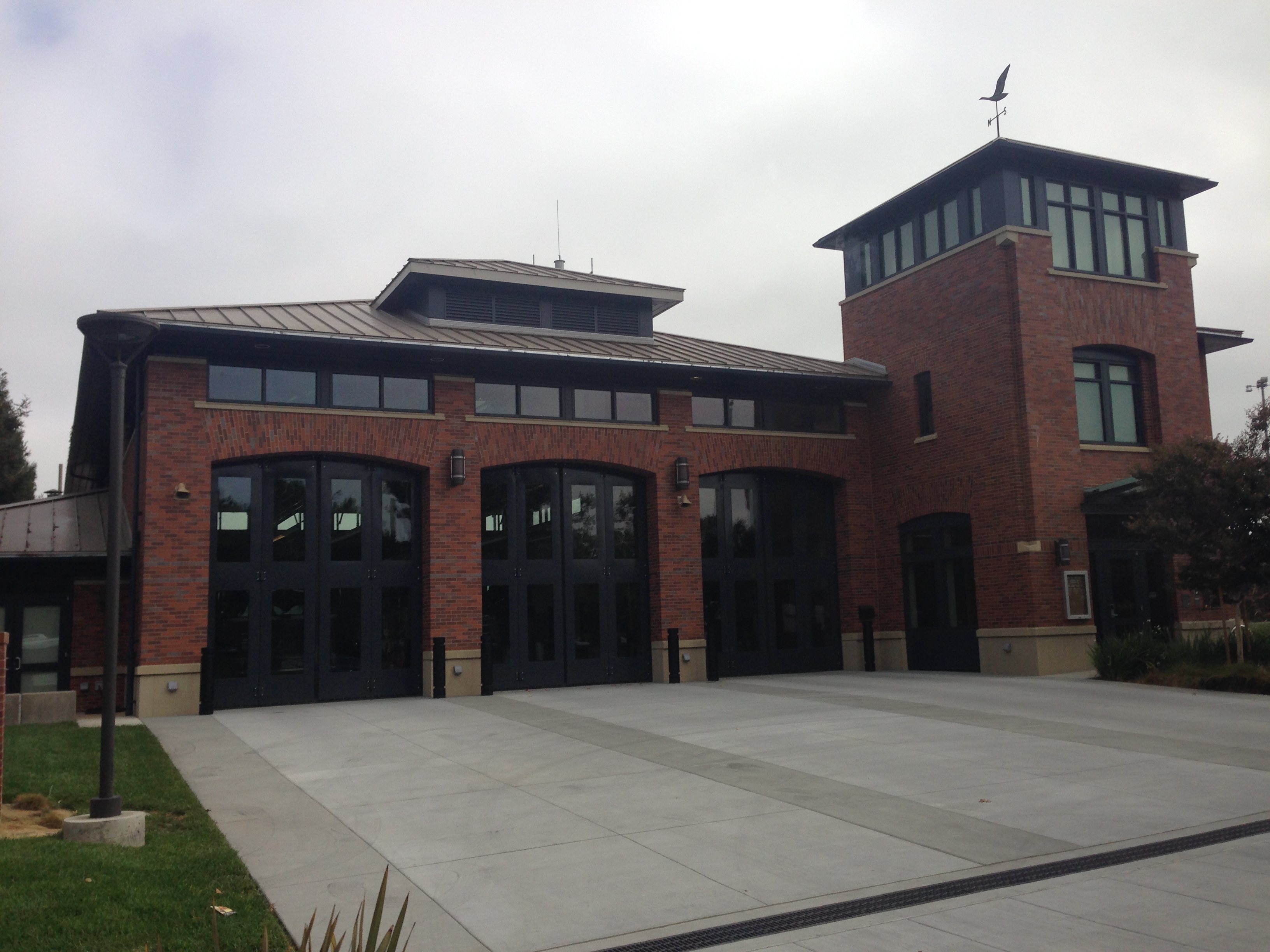 Exterior of a red-brick fire station with arched bay doors and a tower.