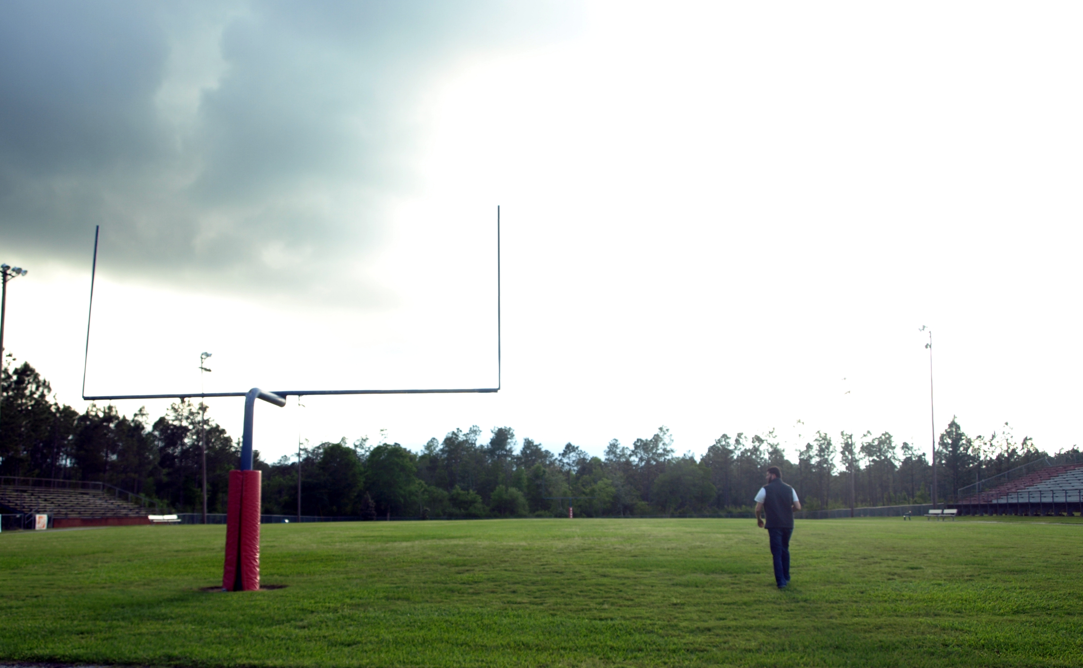 Empty high school football field with red goalposts and bleachers under an overcast sky.