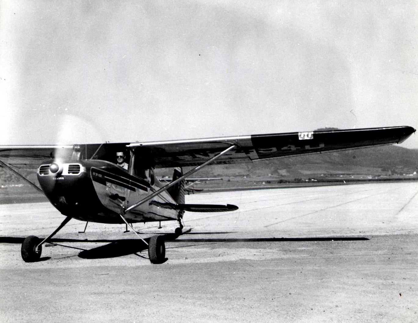 Small single-engine propeller plane taxiing on an airport tarmac, hills in background.
