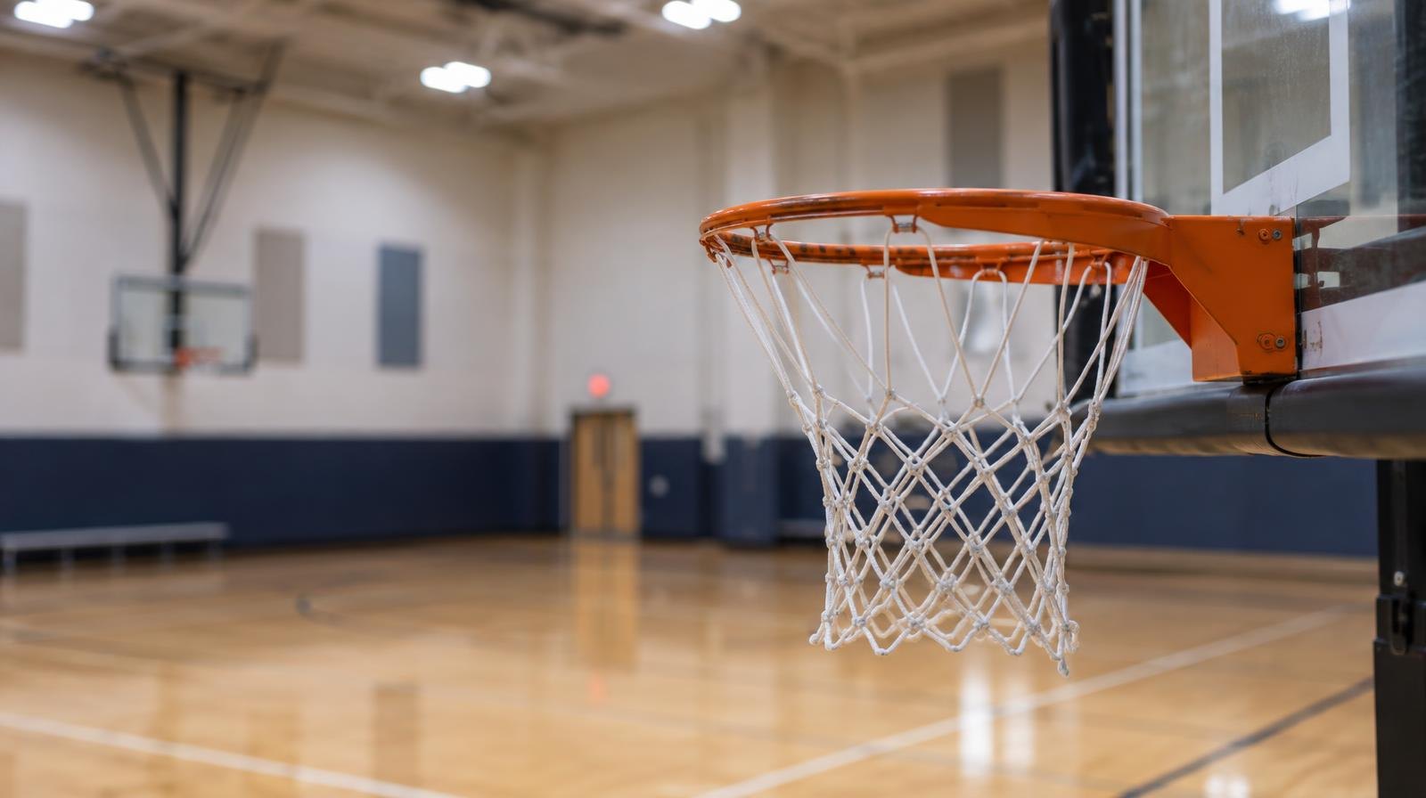 Empty gymnasium interior with a basketball hoop and hardwood court floor.