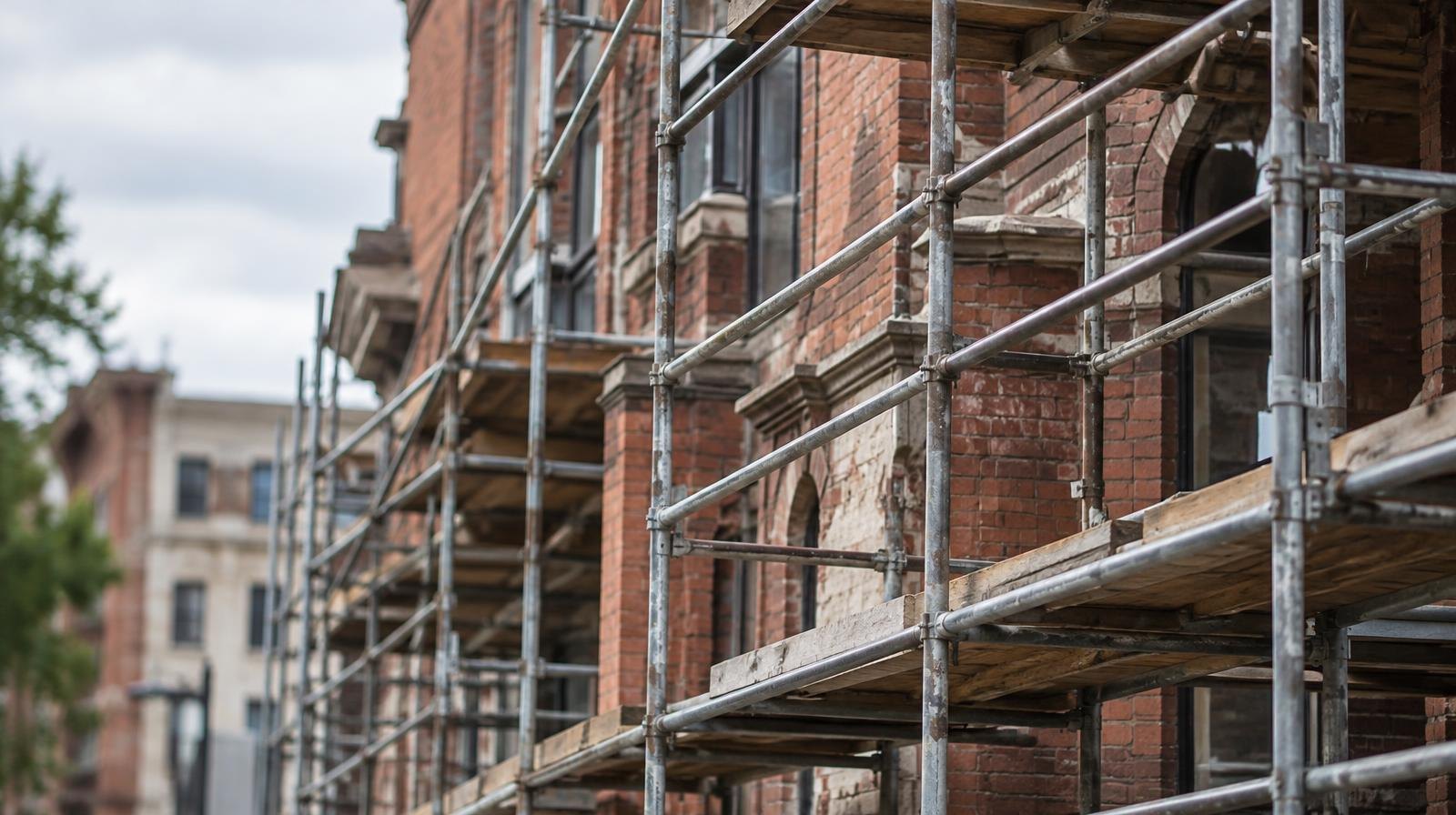 Metal scaffolding covering the brick facade of an older multi-story building.