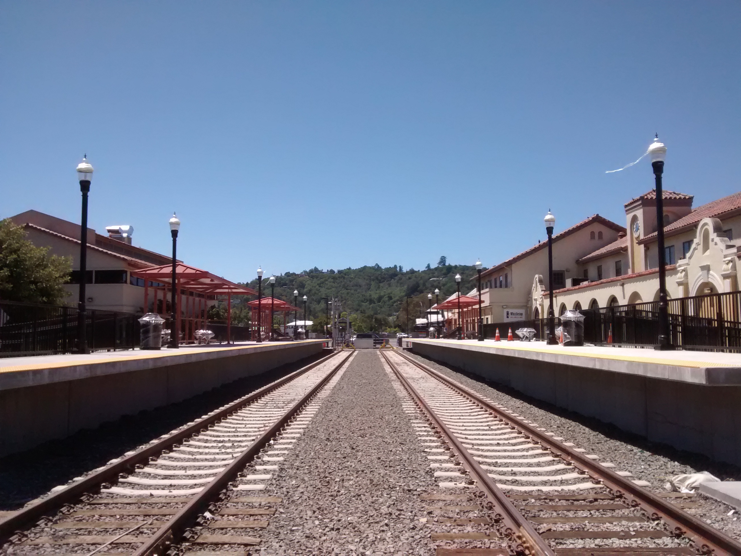 Two parallel rail tracks between station platforms with lamp posts and a station building.