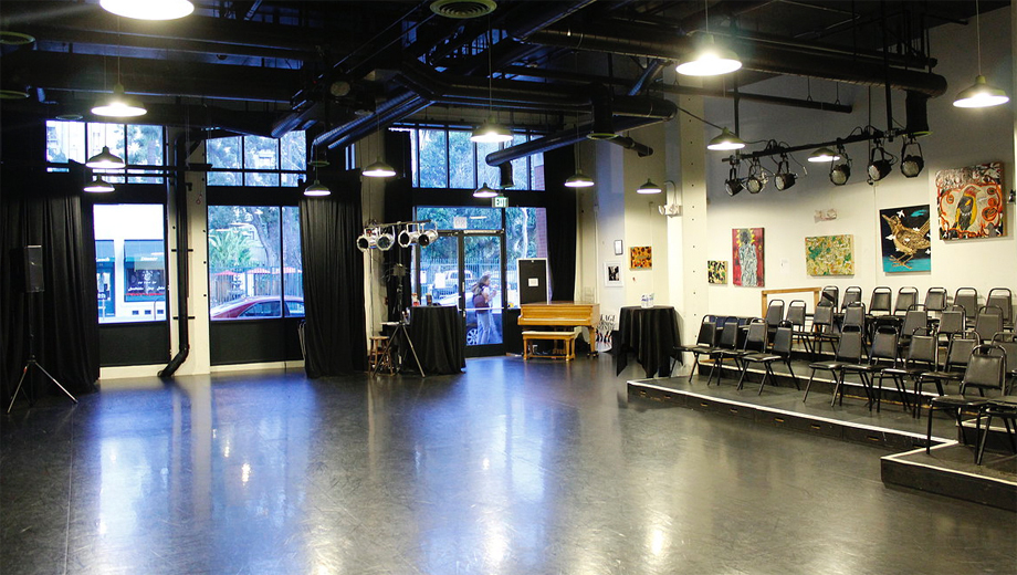 Interior of a black-box theater space with stage lighting rigs and folding chairs.