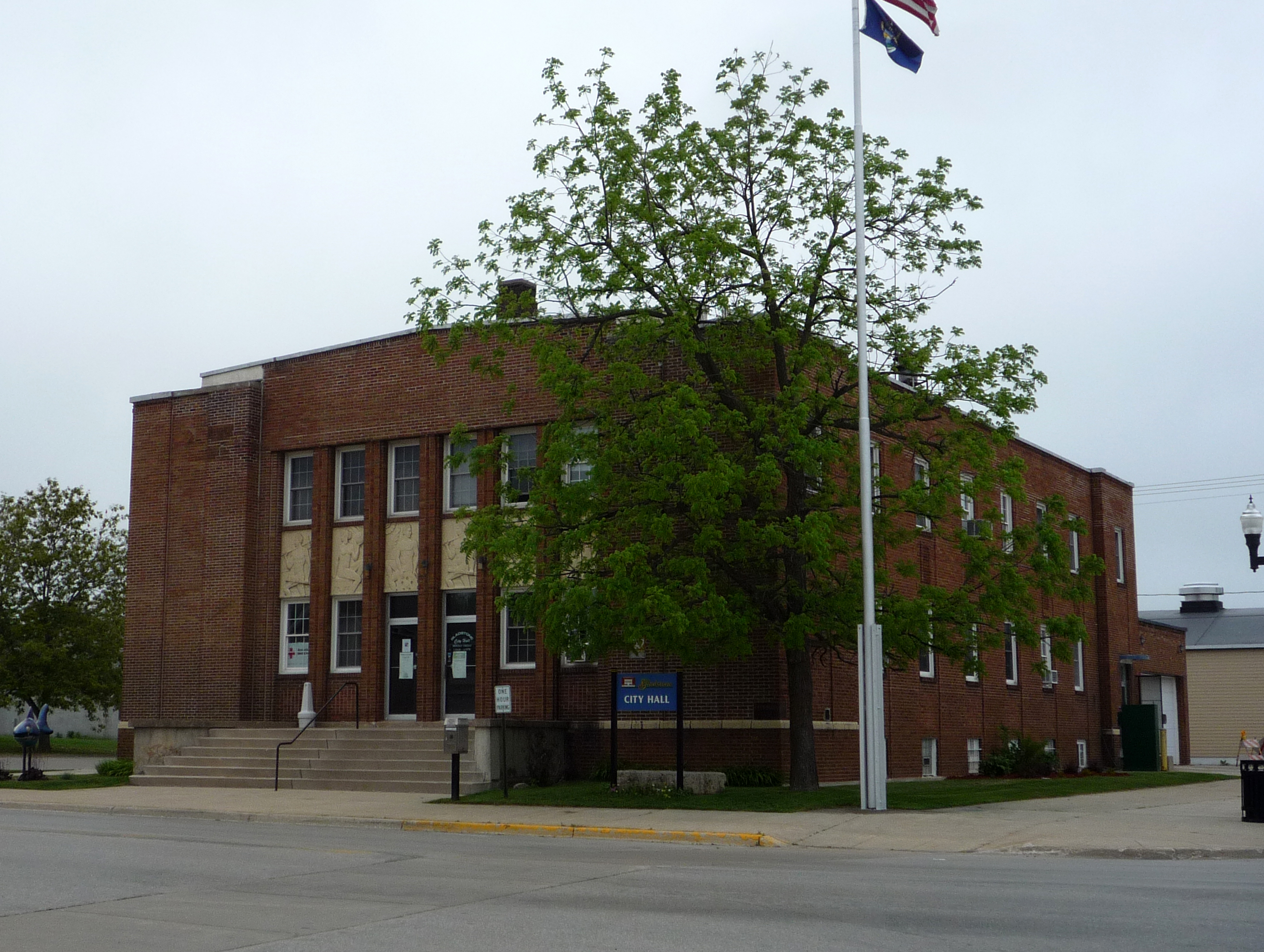 Two-story red brick city hall building with an American flag on a flagpole out front.