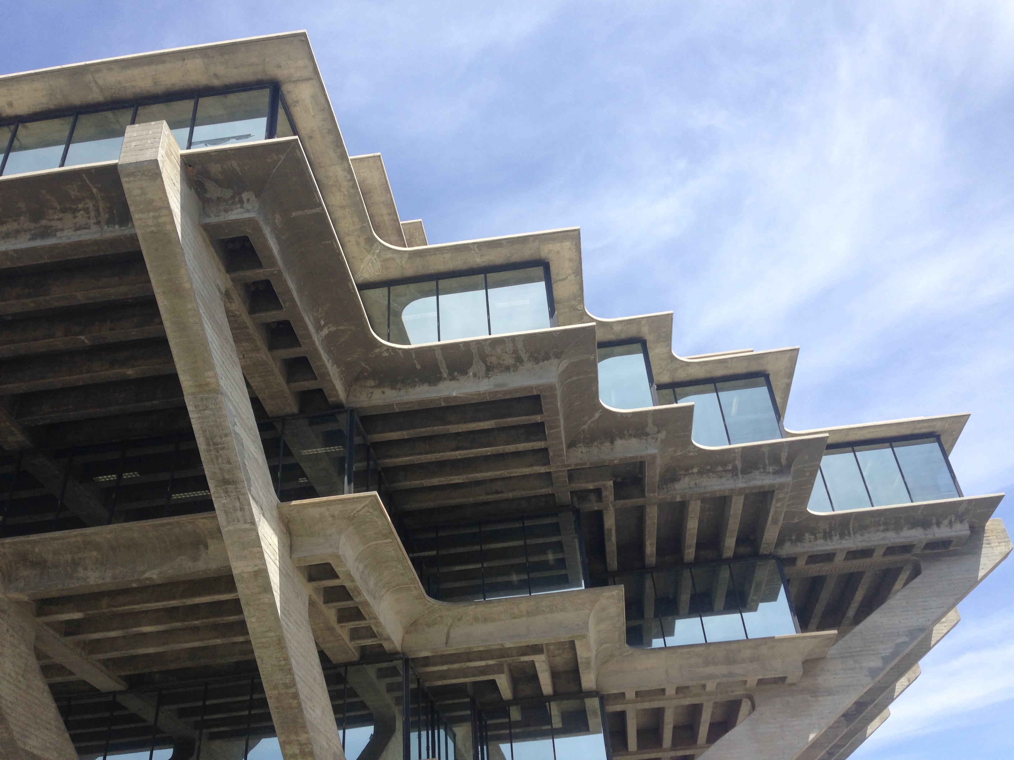 Upward-angle view of a brutalist concrete building with cantilevered floors and large windows.