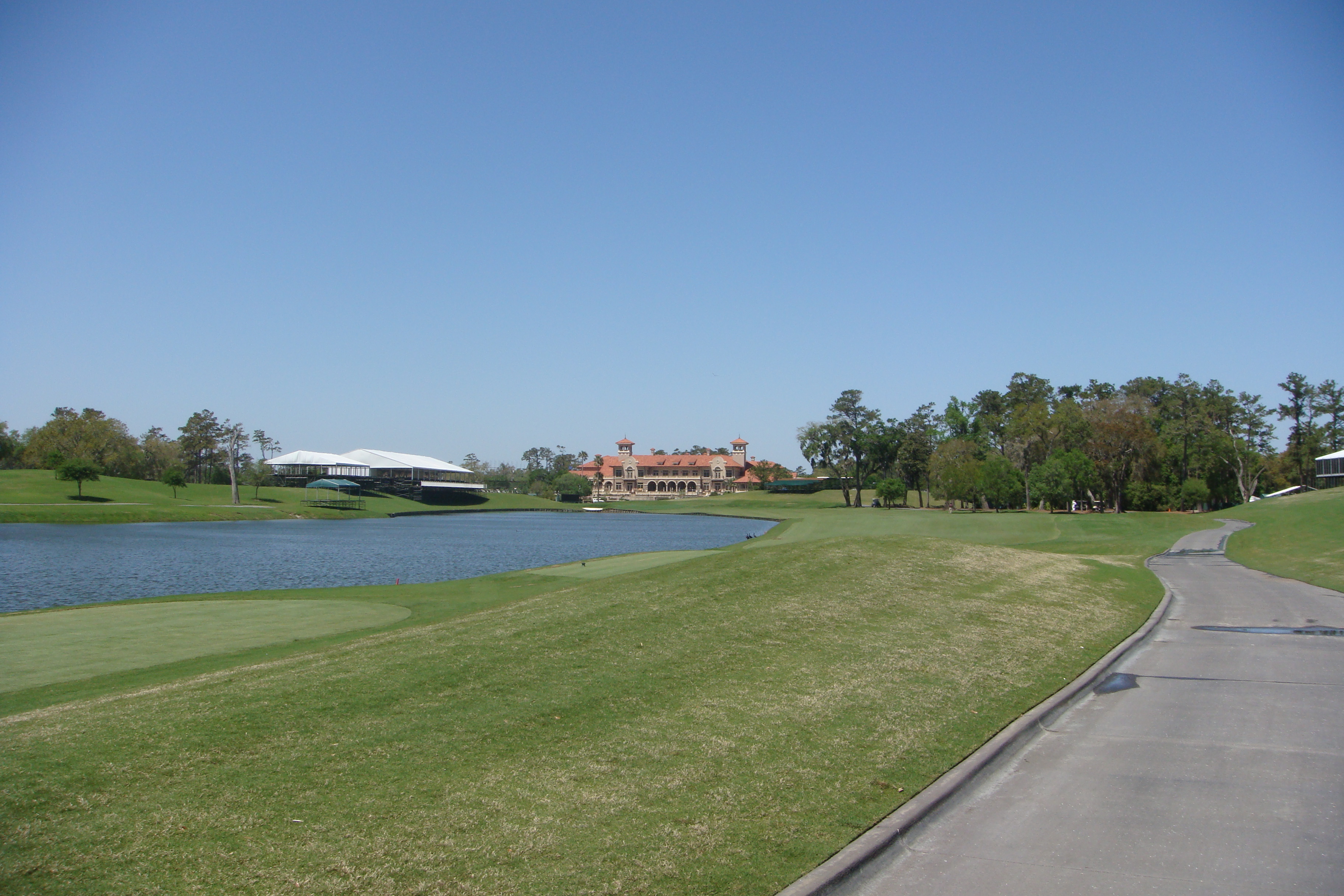 Wide view of a golf course with fairways, a water hazard, and a clubhouse with a red-tiled roof.