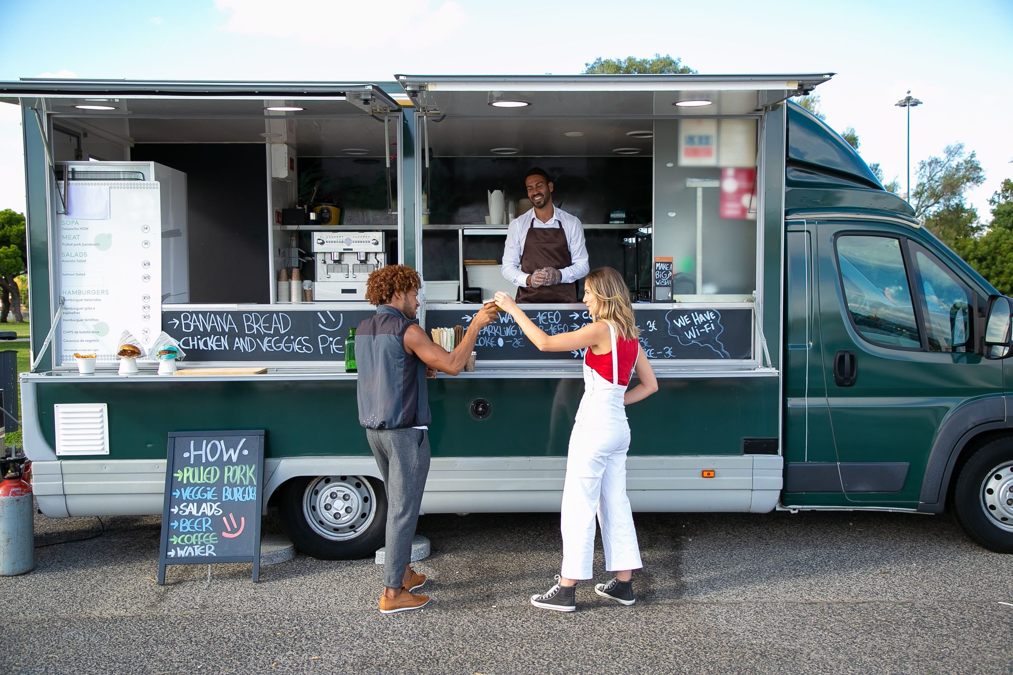 Full body back view full body of multiracial couple toasting with drinks while having lunch at food truck
