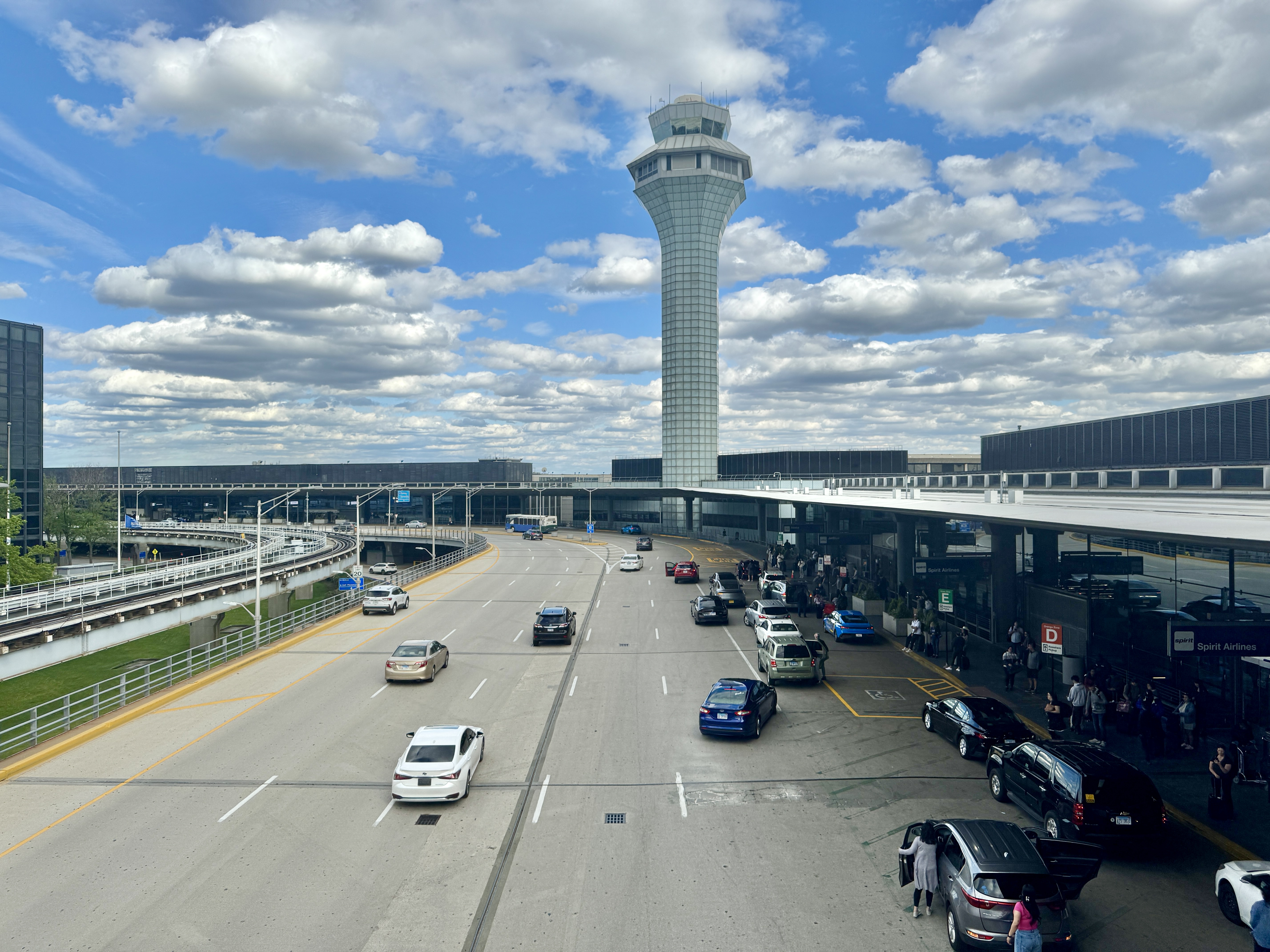 Airport terminal drop-off roadway with a tall air traffic control tower in the background.