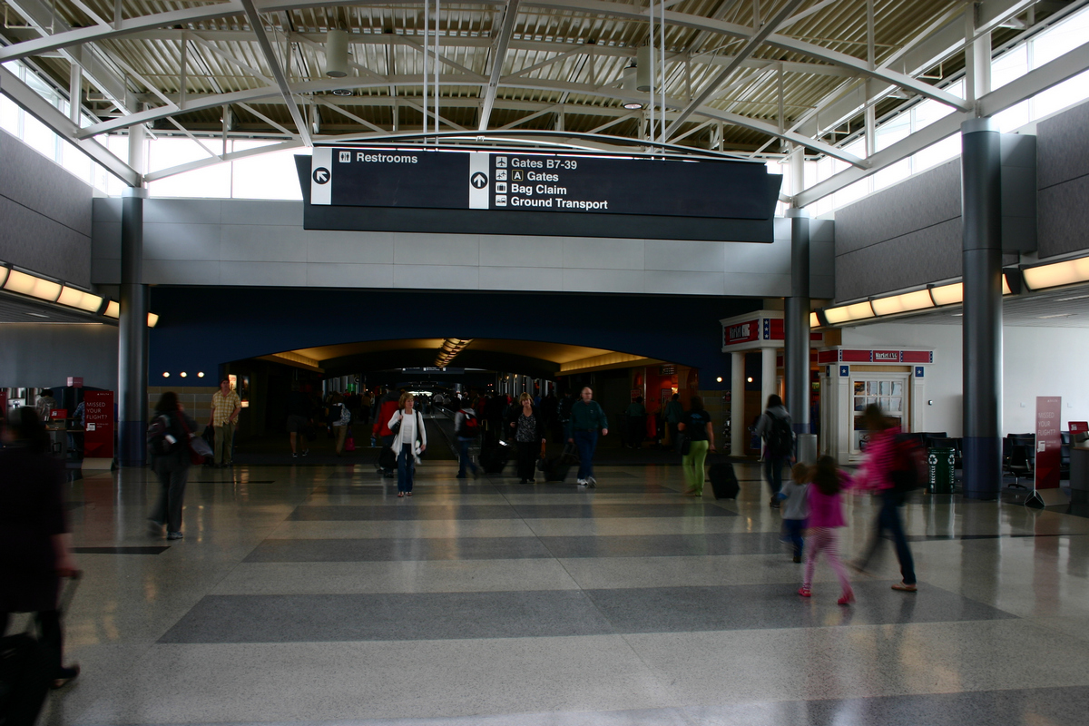 Airport terminal concourse with travelers walking beneath overhead directional signage.