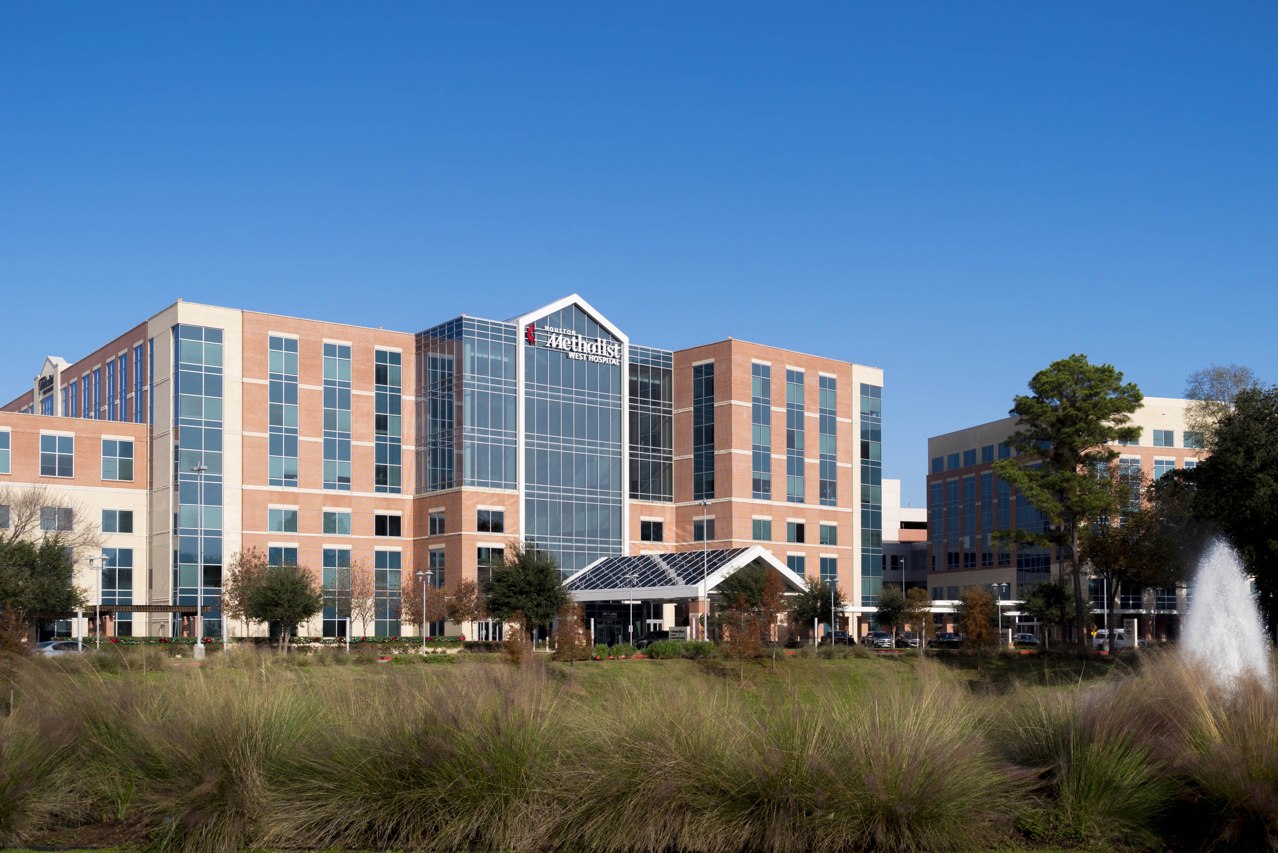 Multi-story brick and glass hospital building with a fountain in front.