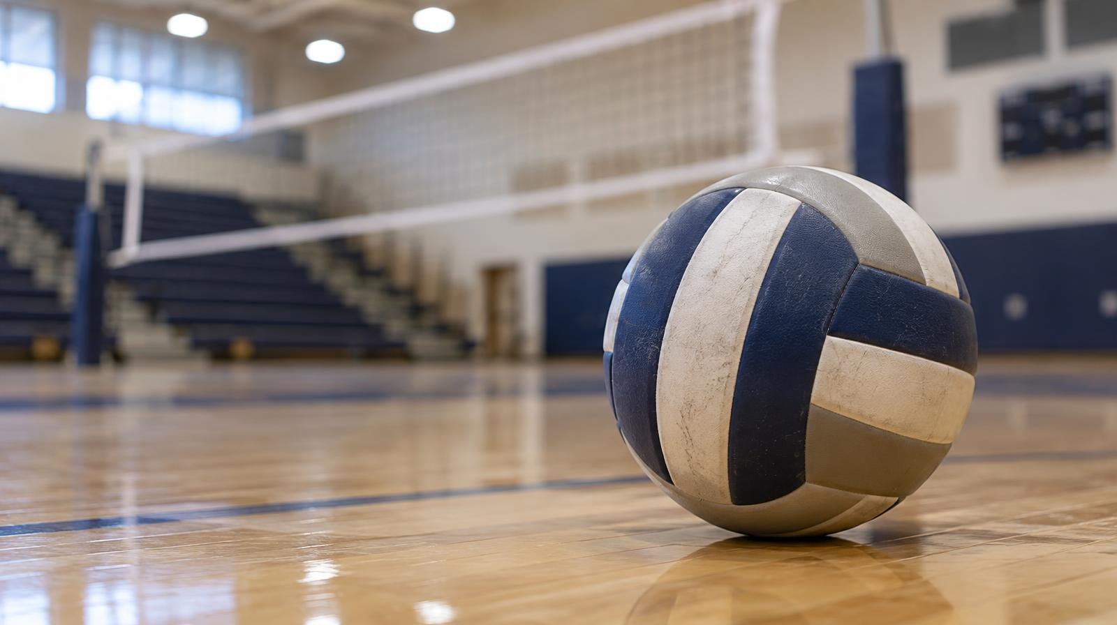 A volleyball resting on a hardwood gym floor near the net.