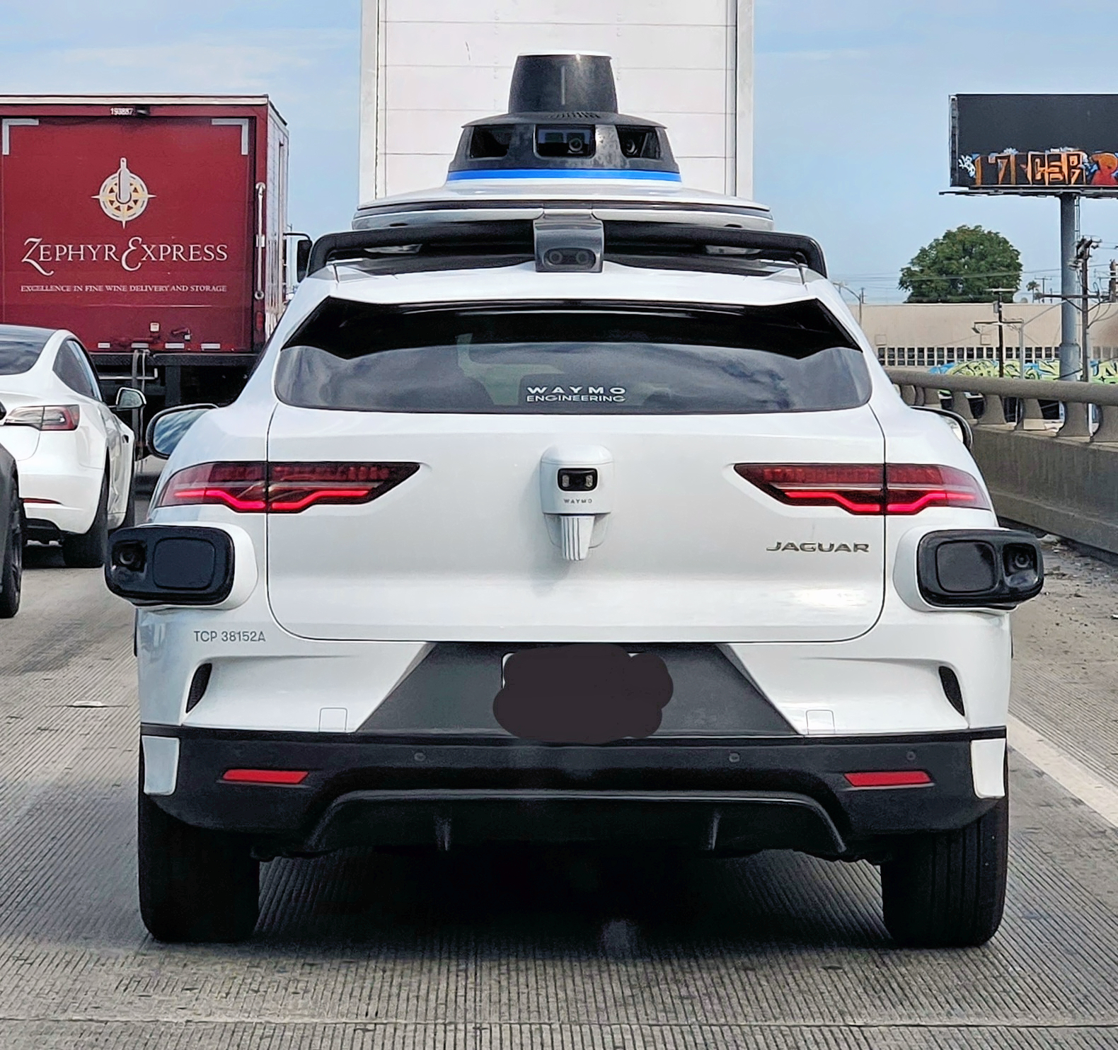 White Waymo vehicle with roof-mounted sensors on a busy freeway.