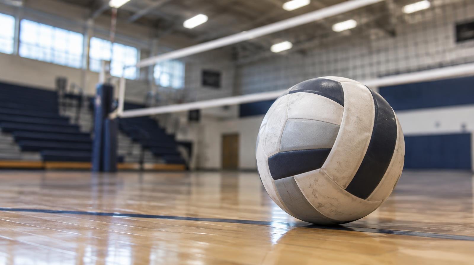A volleyball resting on a hardwood gym floor near the net.