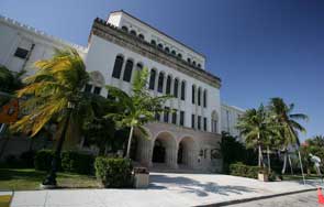 White Mediterranean-style building with arched colonnades and palm trees under a blue sky.