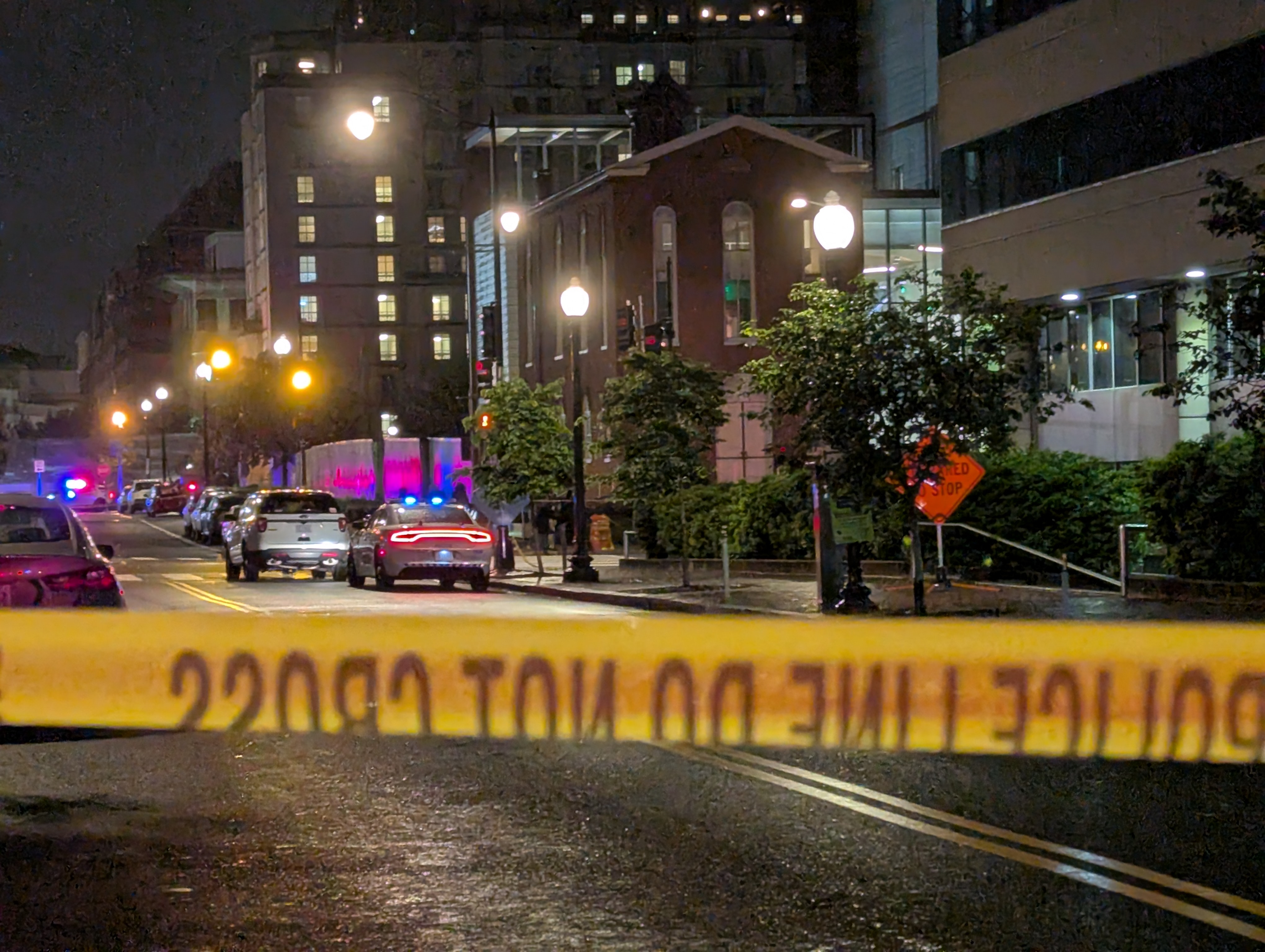 Yellow police tape reading 'Police Line Do Not Cross' at a nighttime crime scene with flashing police lights.