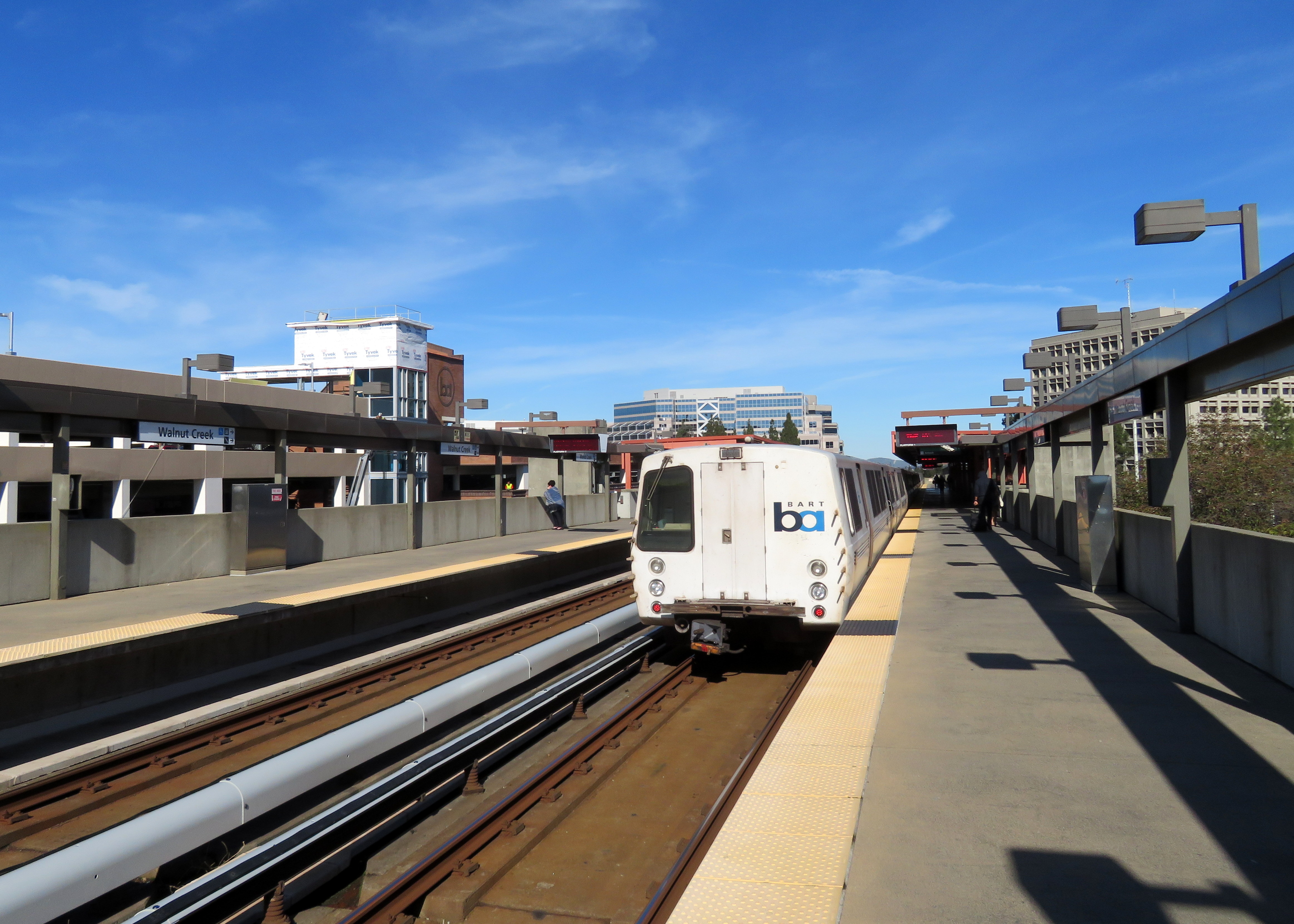 An Antioch-bound BART train at an elevated station platform under blue sky.
