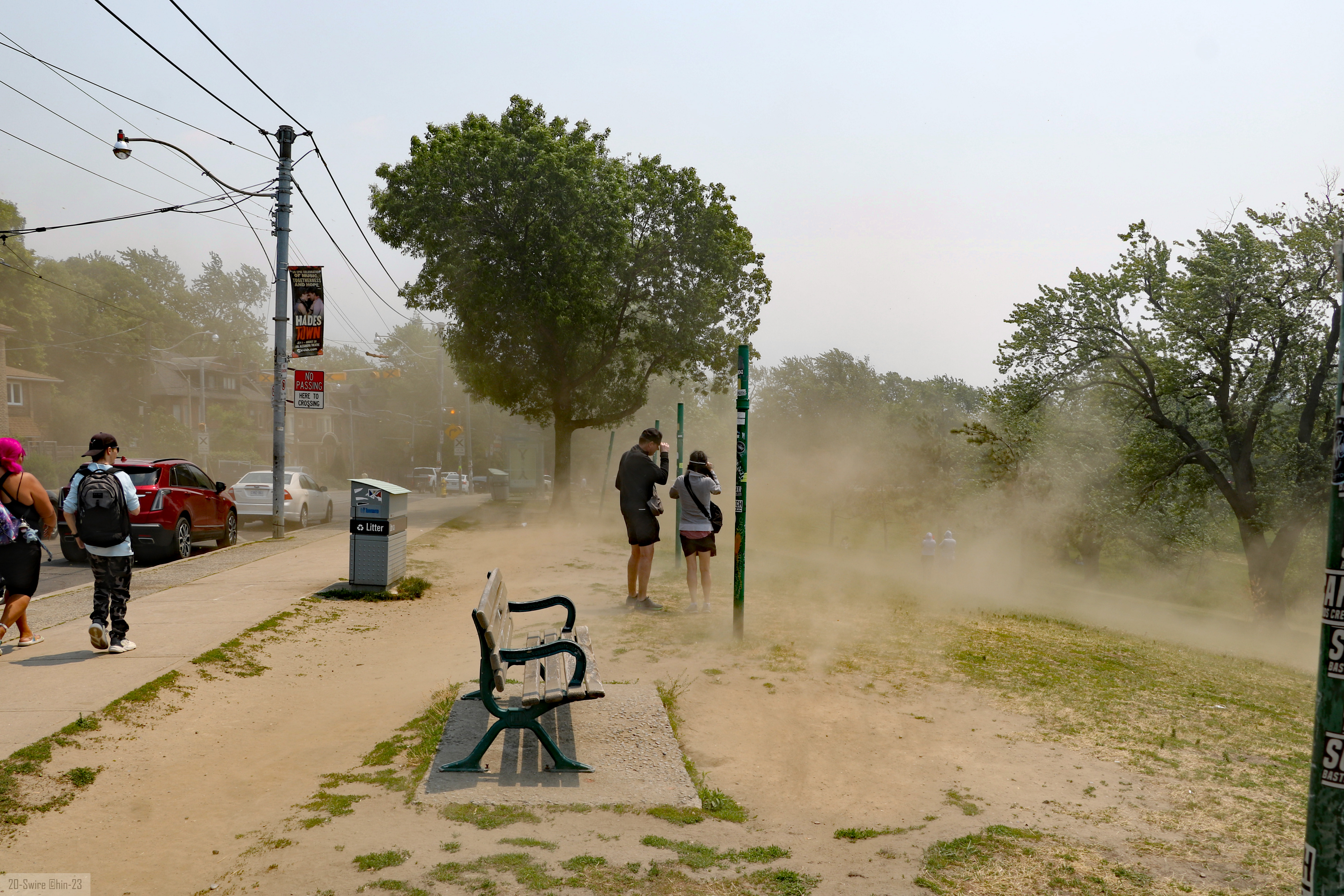 Pedestrians walk along a hazy sidewalk with severely reduced visibility from smoke.
