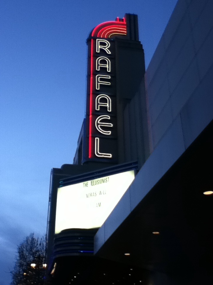 Theater exterior at dusk with red and white neon vertical sign and lit marquee.