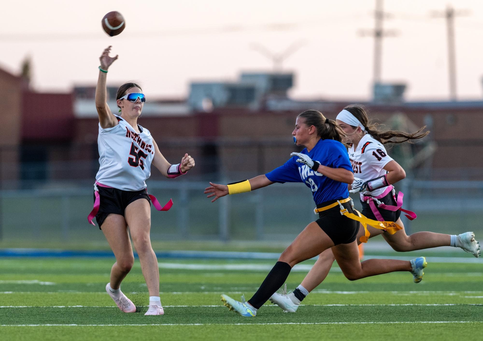 A player in a white jersey with pink flags throws a football on a turf field.