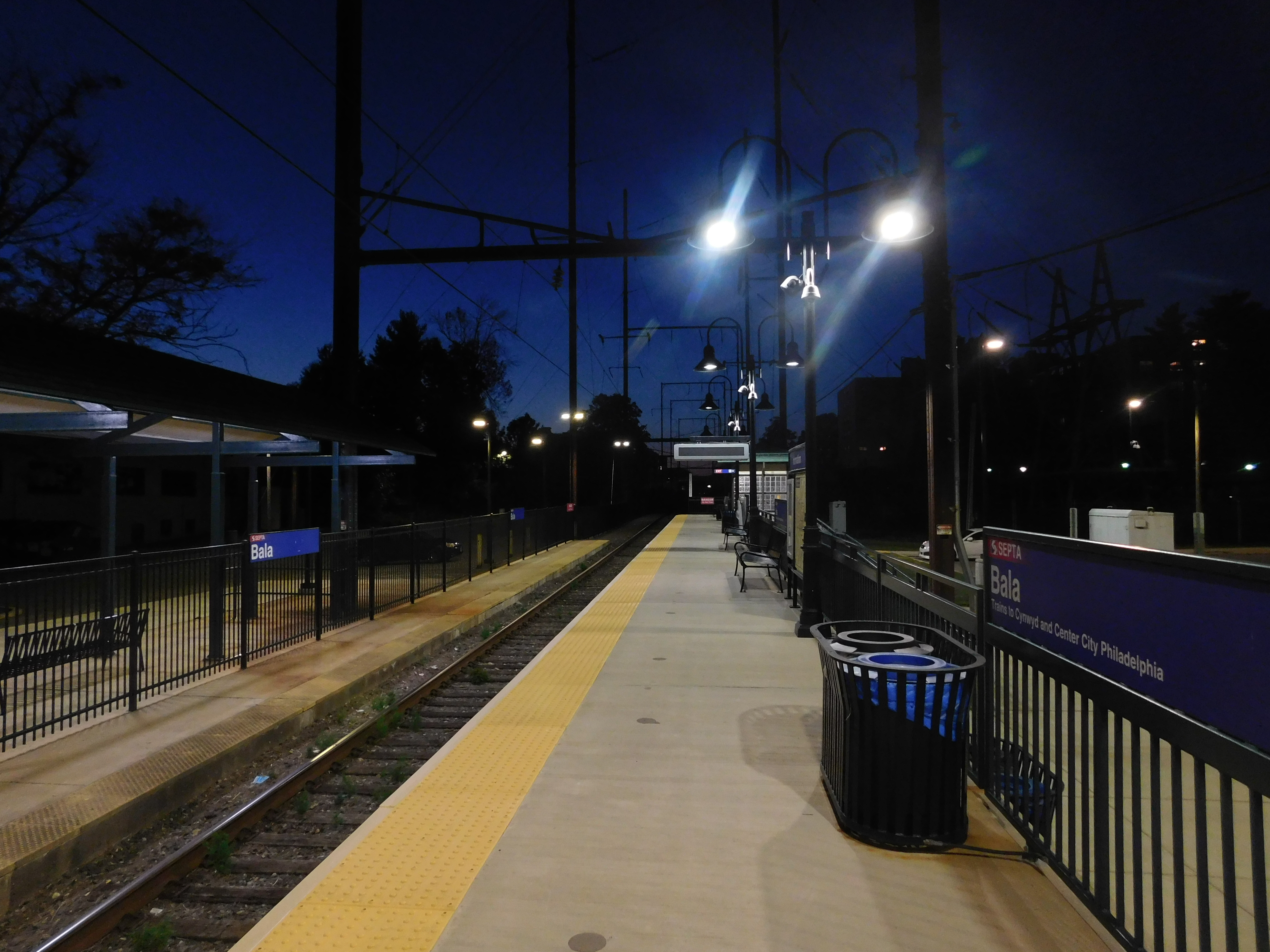 A SEPTA commuter rail platform at night with overhead wires and a station sign reading 'Bala'.